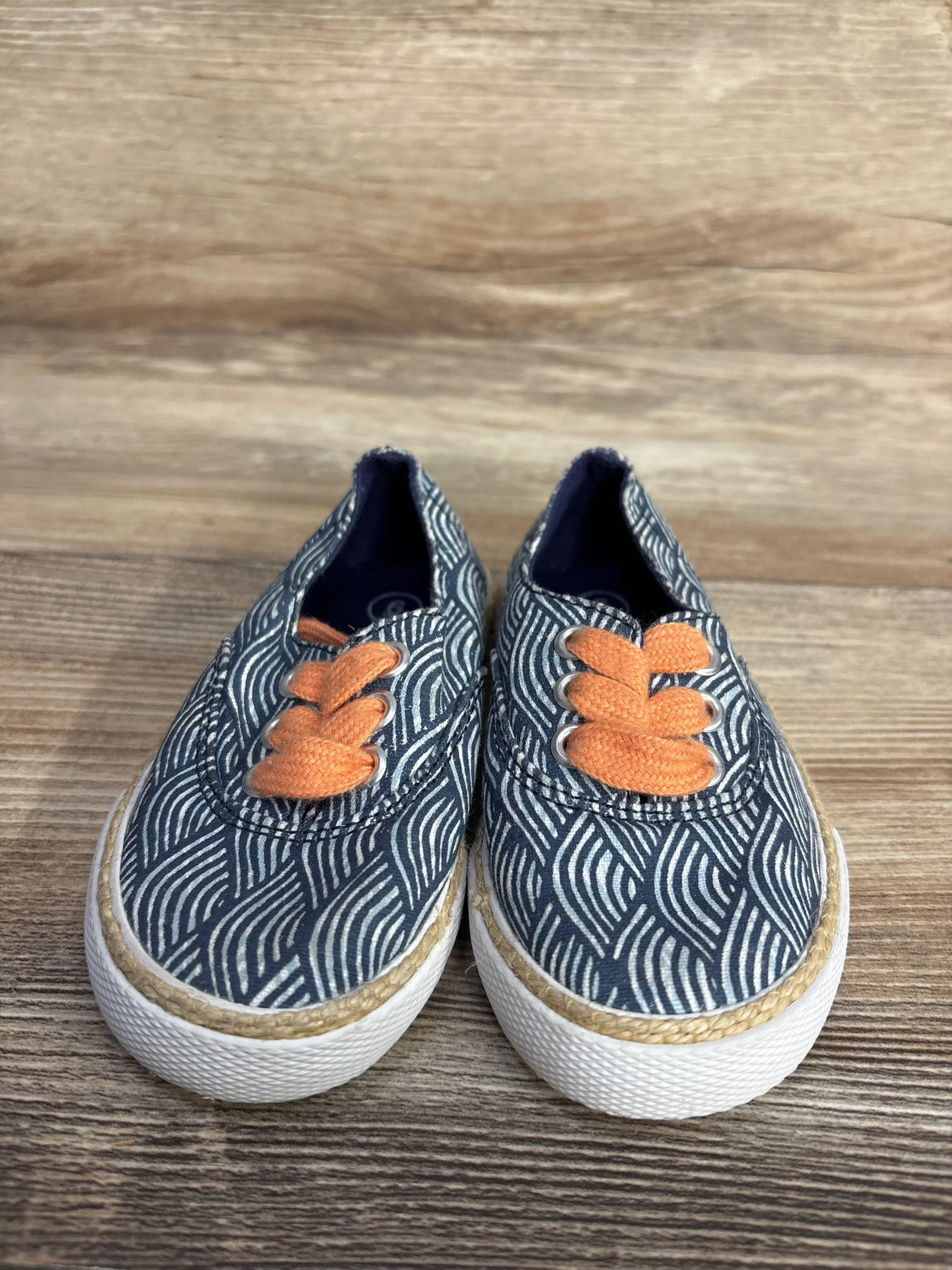 Blue patterned canvas sneakers with orange laces and white soles on a wooden floor