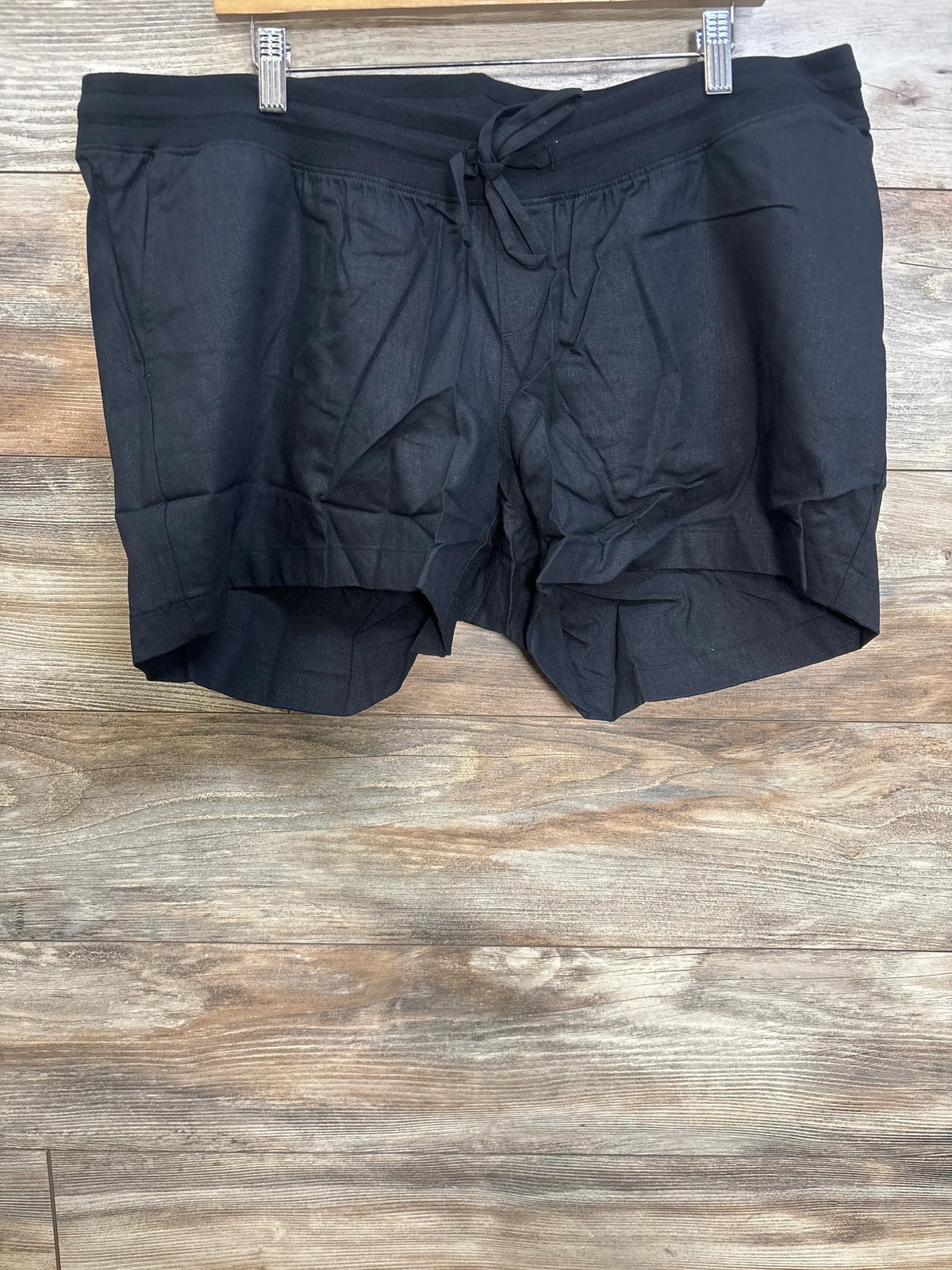 Front view of Gap black maternity linen-blend shorts with elastic under-belly waist, drawcords, and slant pockets on wood