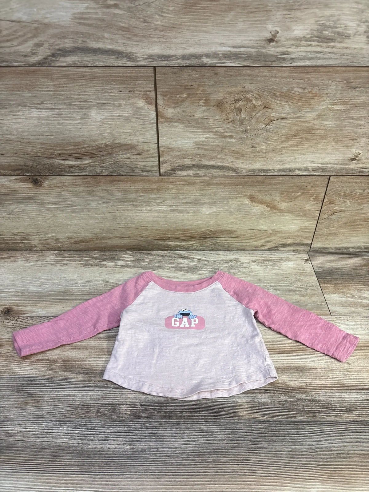Front view of Baby Gap raglan long-sleeve t-shirt with pink sleeves and Cookie Monster above GAP logo, laid flat on wood floor