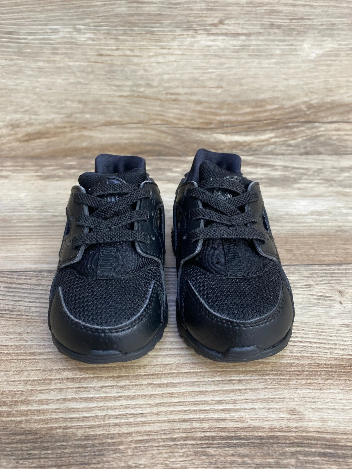 Front view of Nike Air Huarache Run toddler sneakers, size 5C, showing black mesh toe, leather overlays, and laces on light wood floor background