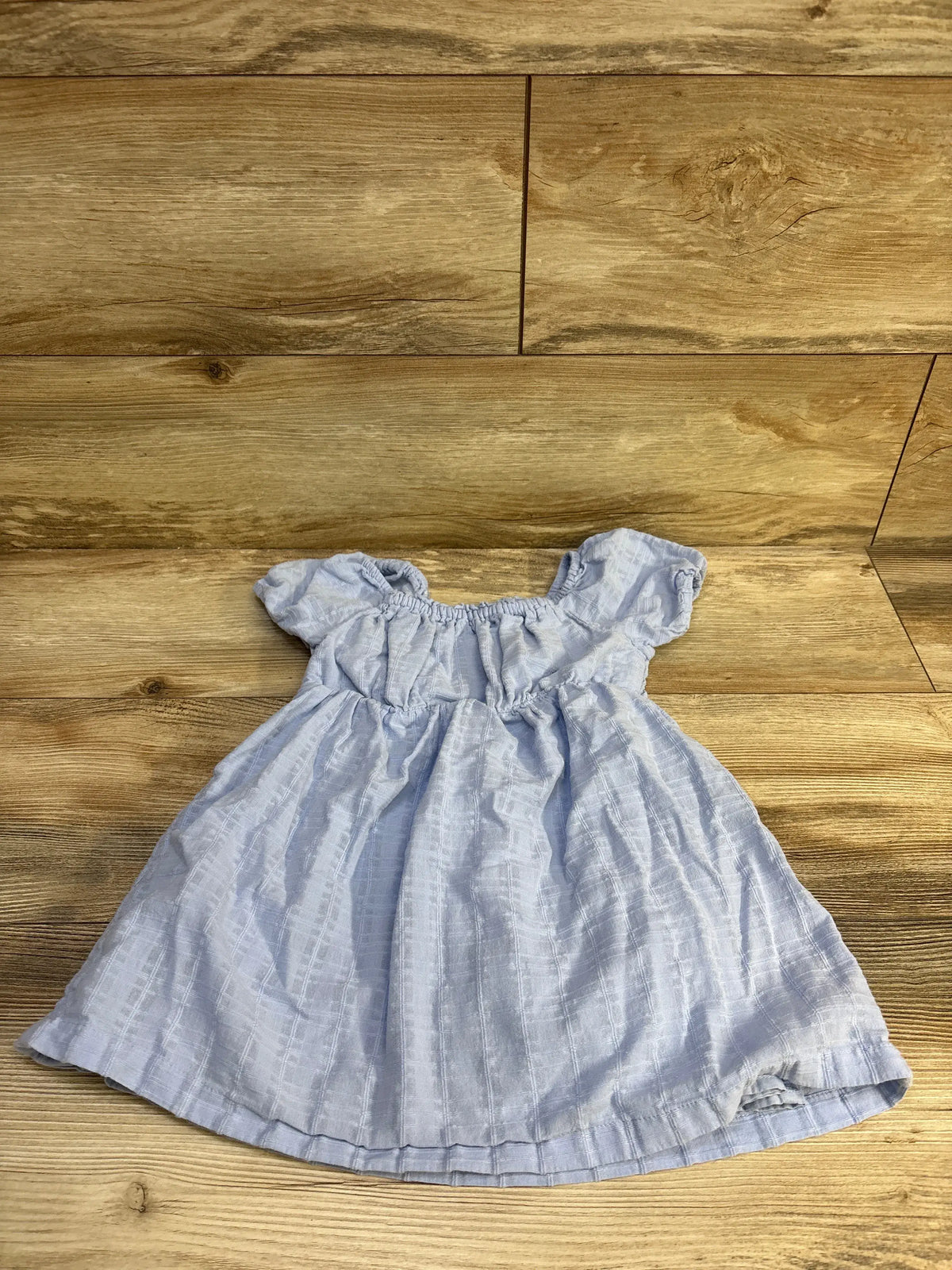 Front flat lay of Baby Gap smocked blue toddler dress showing smocked bodice, puff sleeves, textured fabric on wooden floor