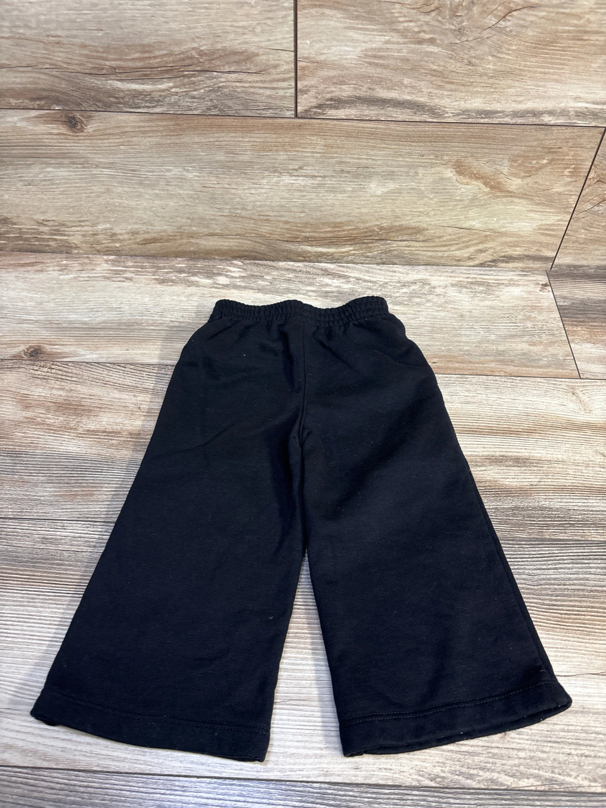Flat lay of Nike black wide-leg joggers size 18 months showing elastic waistband and wide legs on light wood floor