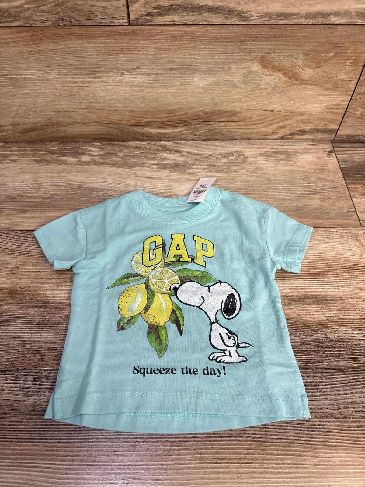 Front view of Baby Gap Snoopy Squeeze The Day shirt showcasing a lemon graphic on a blue shirt over a wood floor