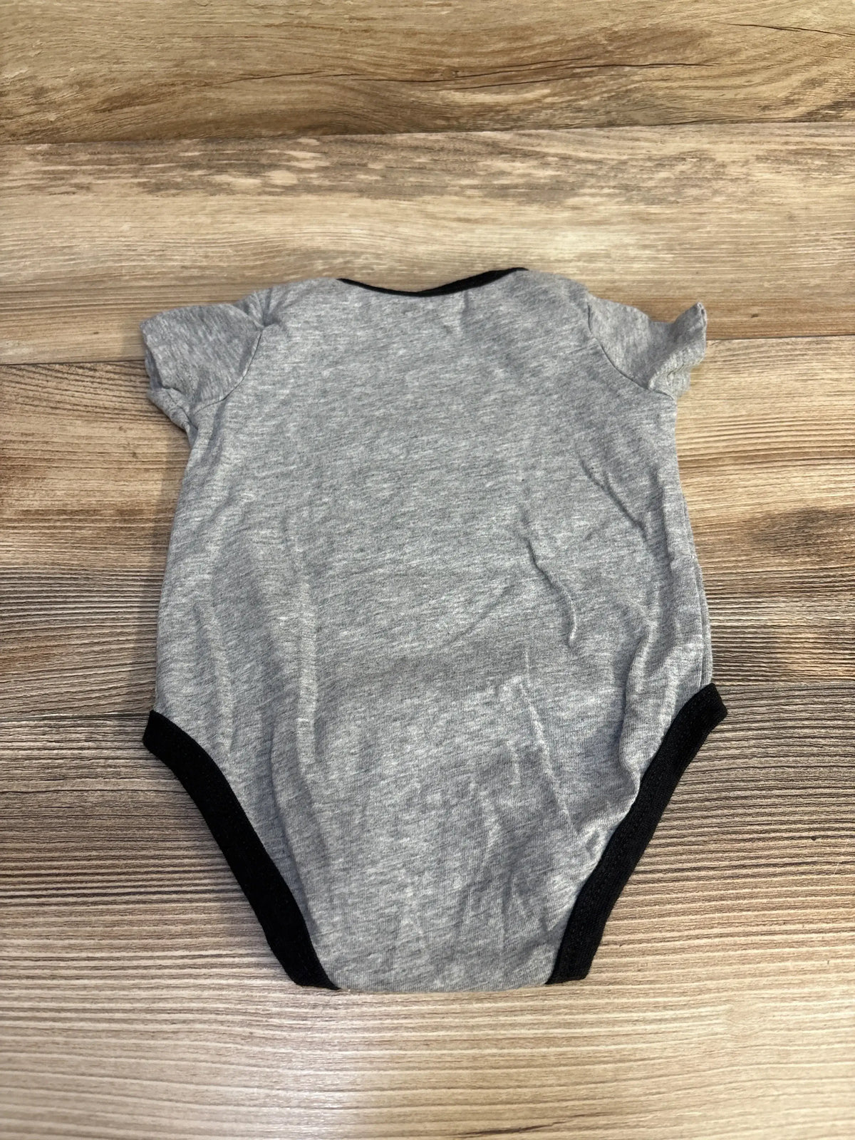 Back view of grey Nike baby bodysuit showcasing black trim and short sleeves laid flat on a wood surface