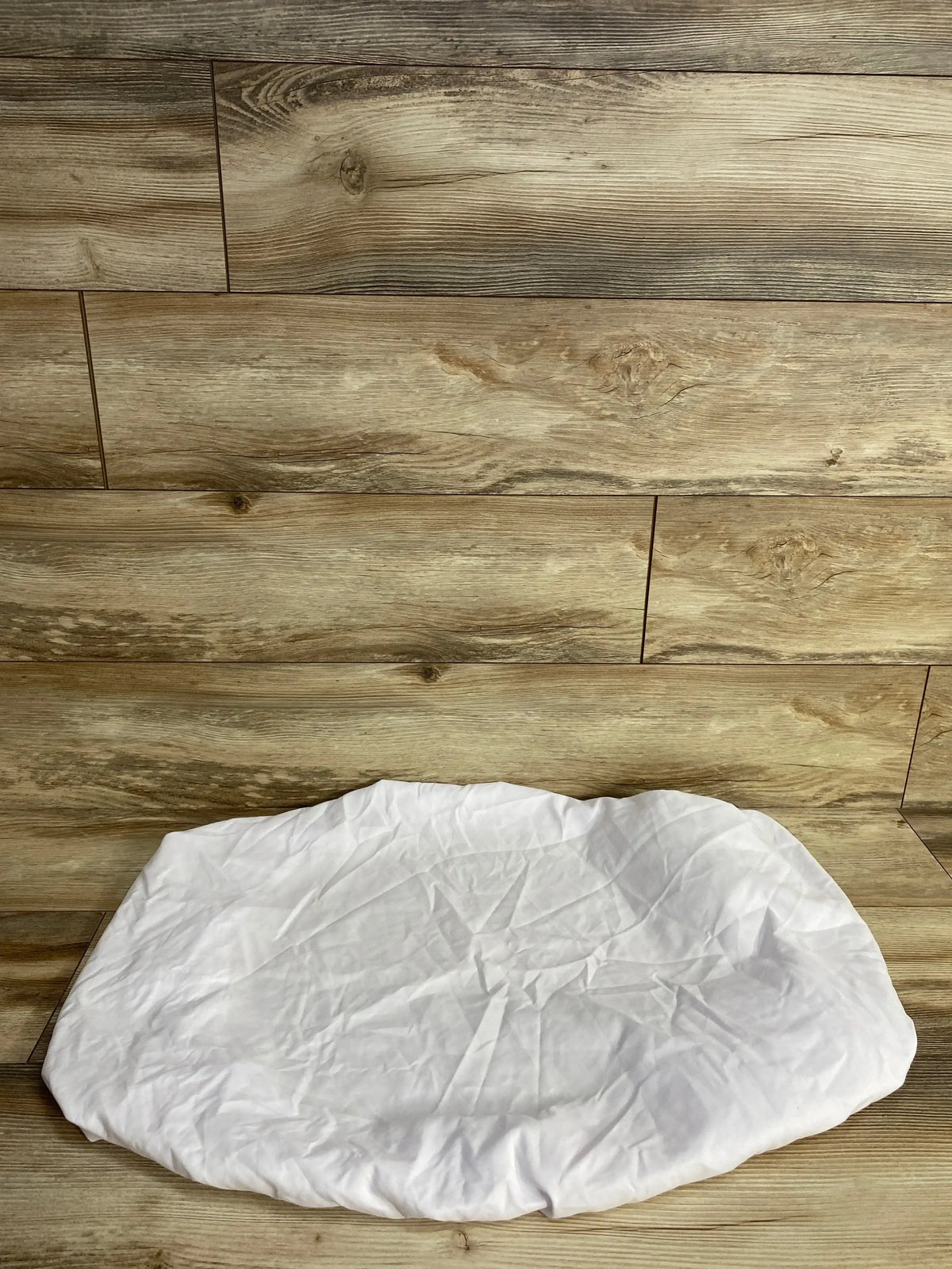 Flat lay of Dream On Me fitted bassinet sheet in white showing fitted oval shape on wood plank floor
