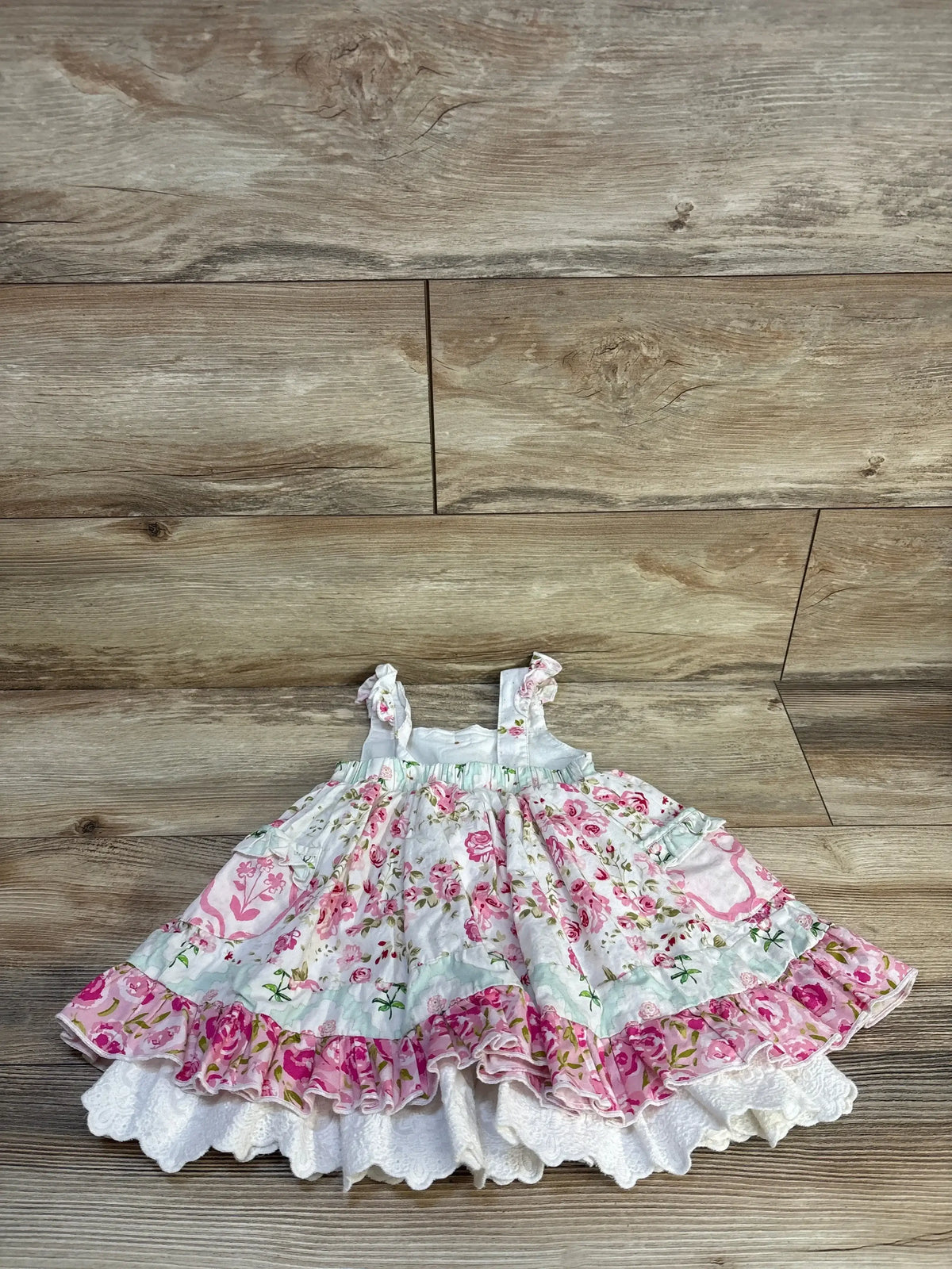Flat lay of Sweet Honey sleeveless girls floral dress size 3T showcasing ruffled hem and lace trim on wood floor