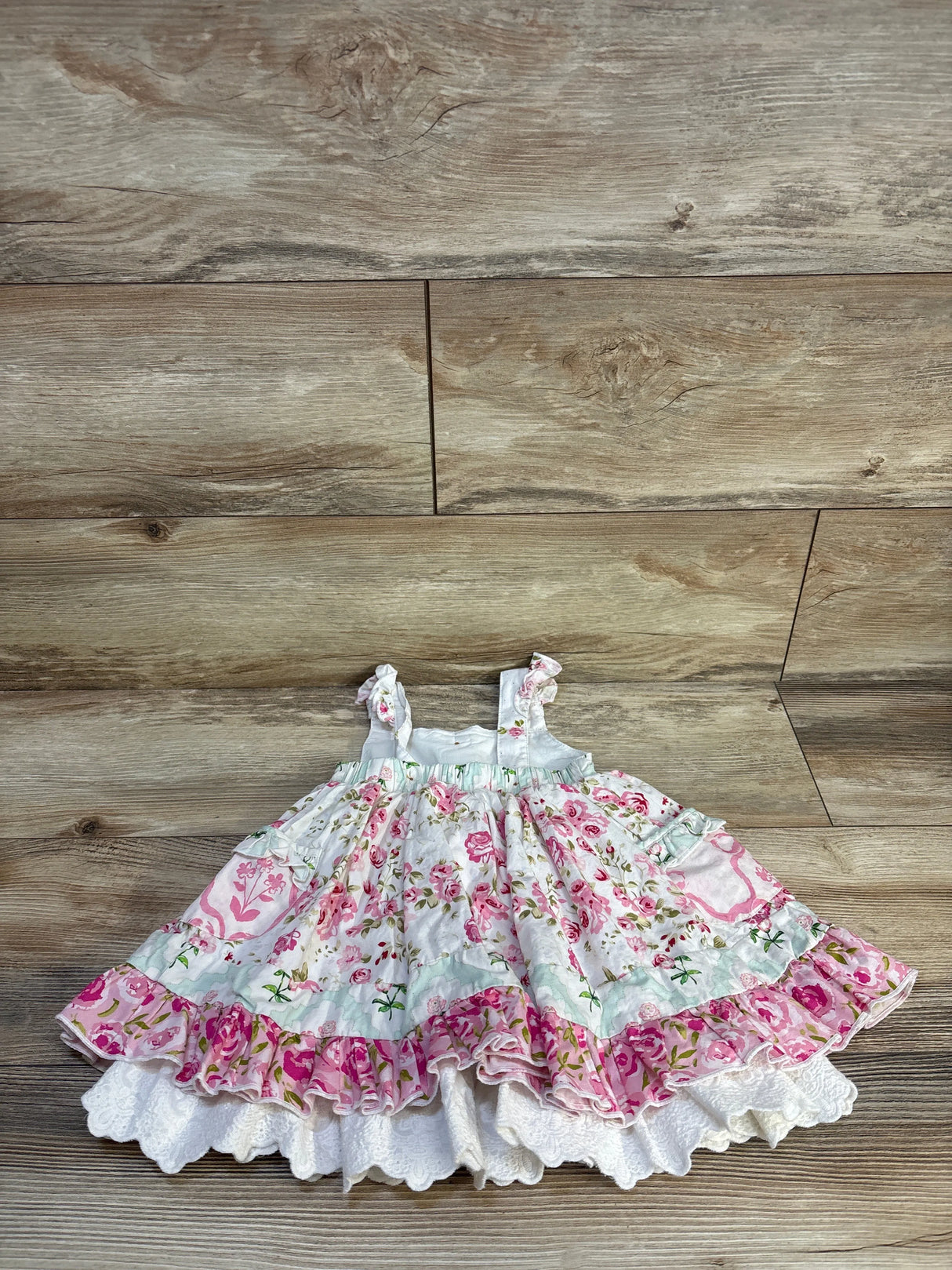 Pink floral baby dress with ruffles, laid on wood floor, kids clothing resale