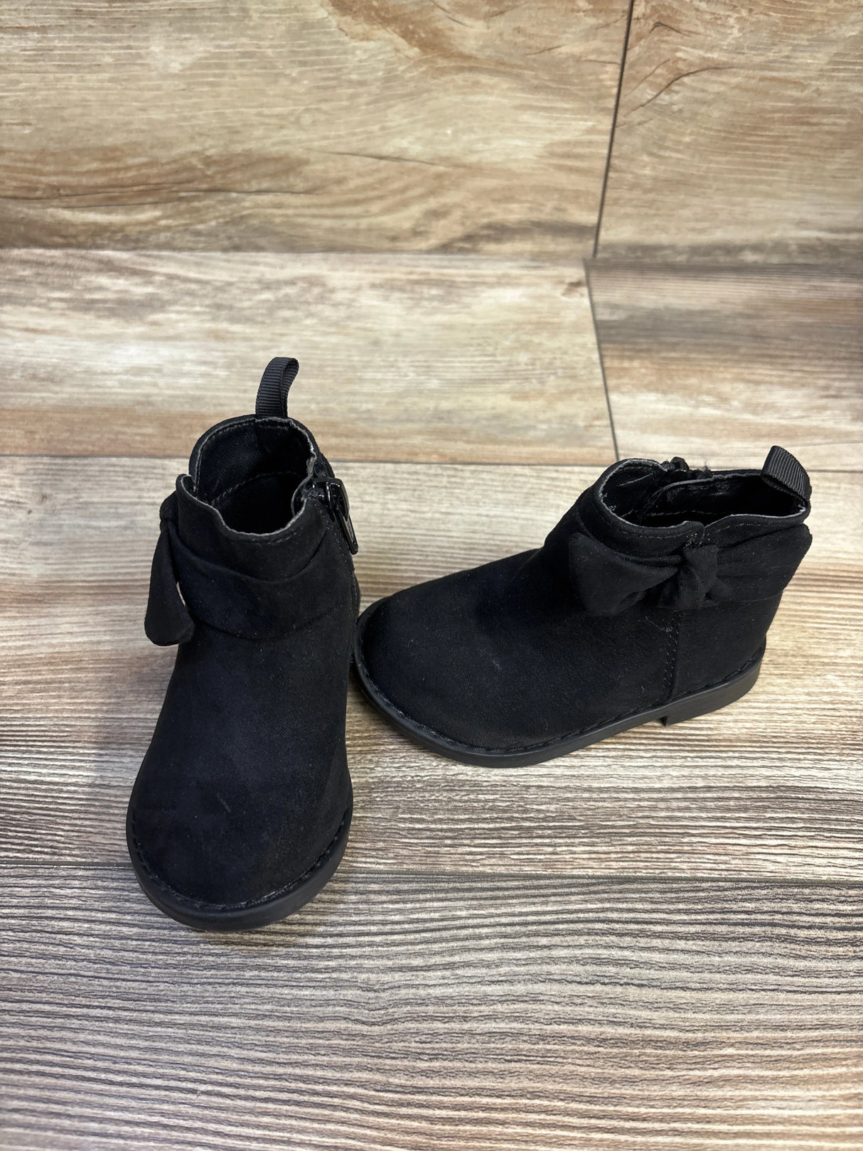 Angled view of Baby Gap black baby ankle boots showing side bow and zipper on wood plank background
