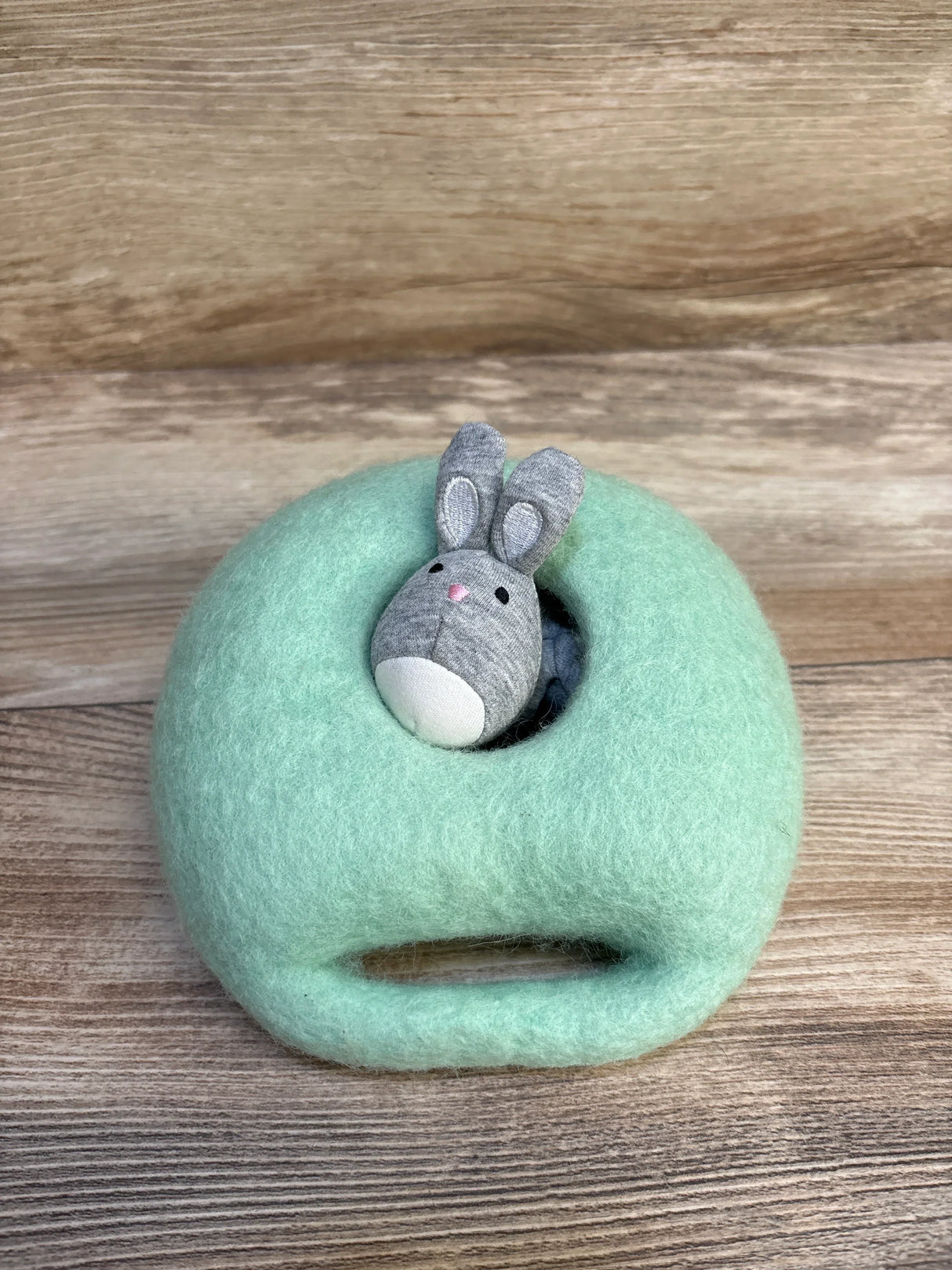 Plush bunny toy peeking out of a soft mint green felted pouch on a wooden surface