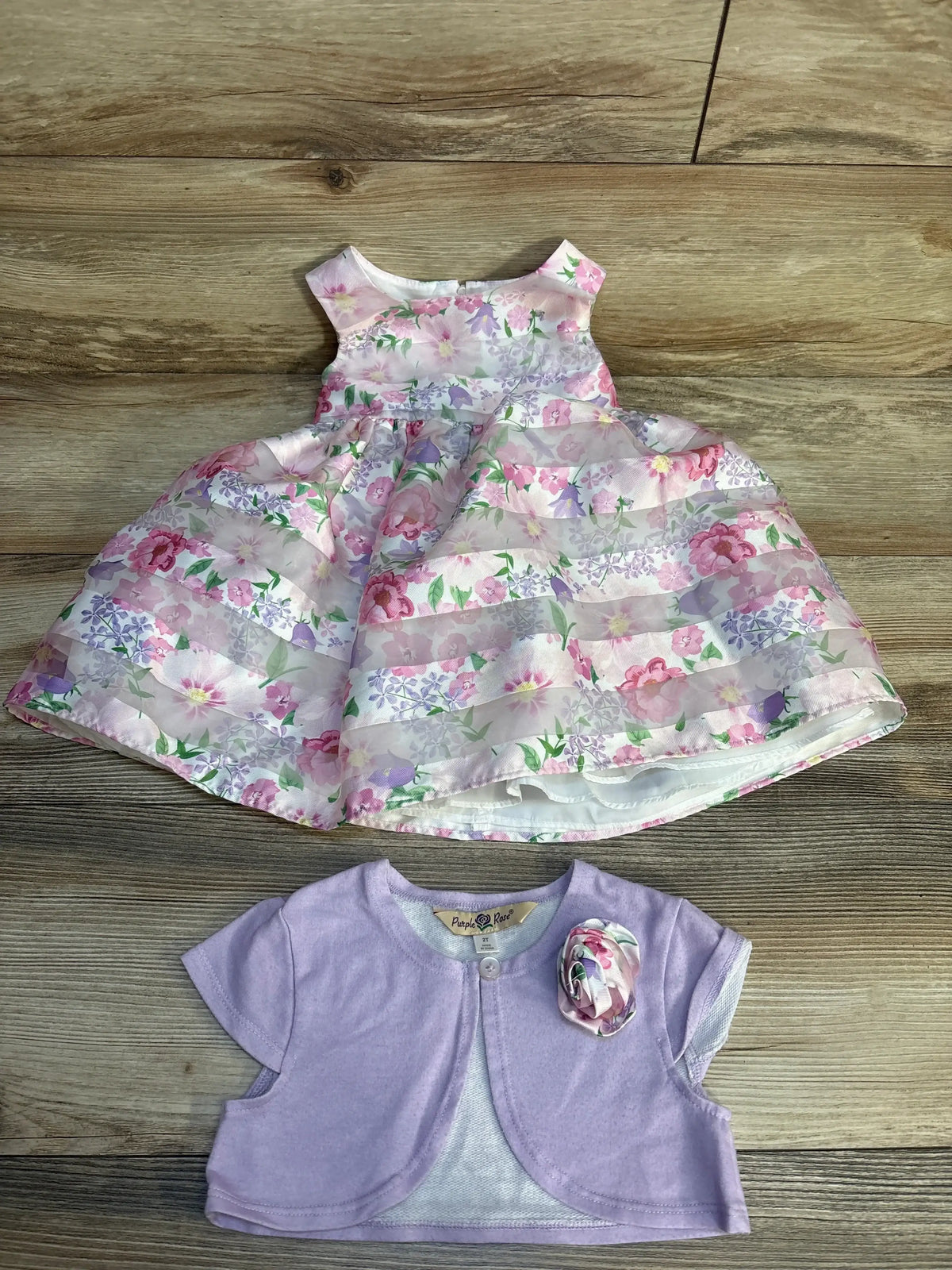 Girls’ floral sleeveless dress with lilac bolero on wood background, spring outfit