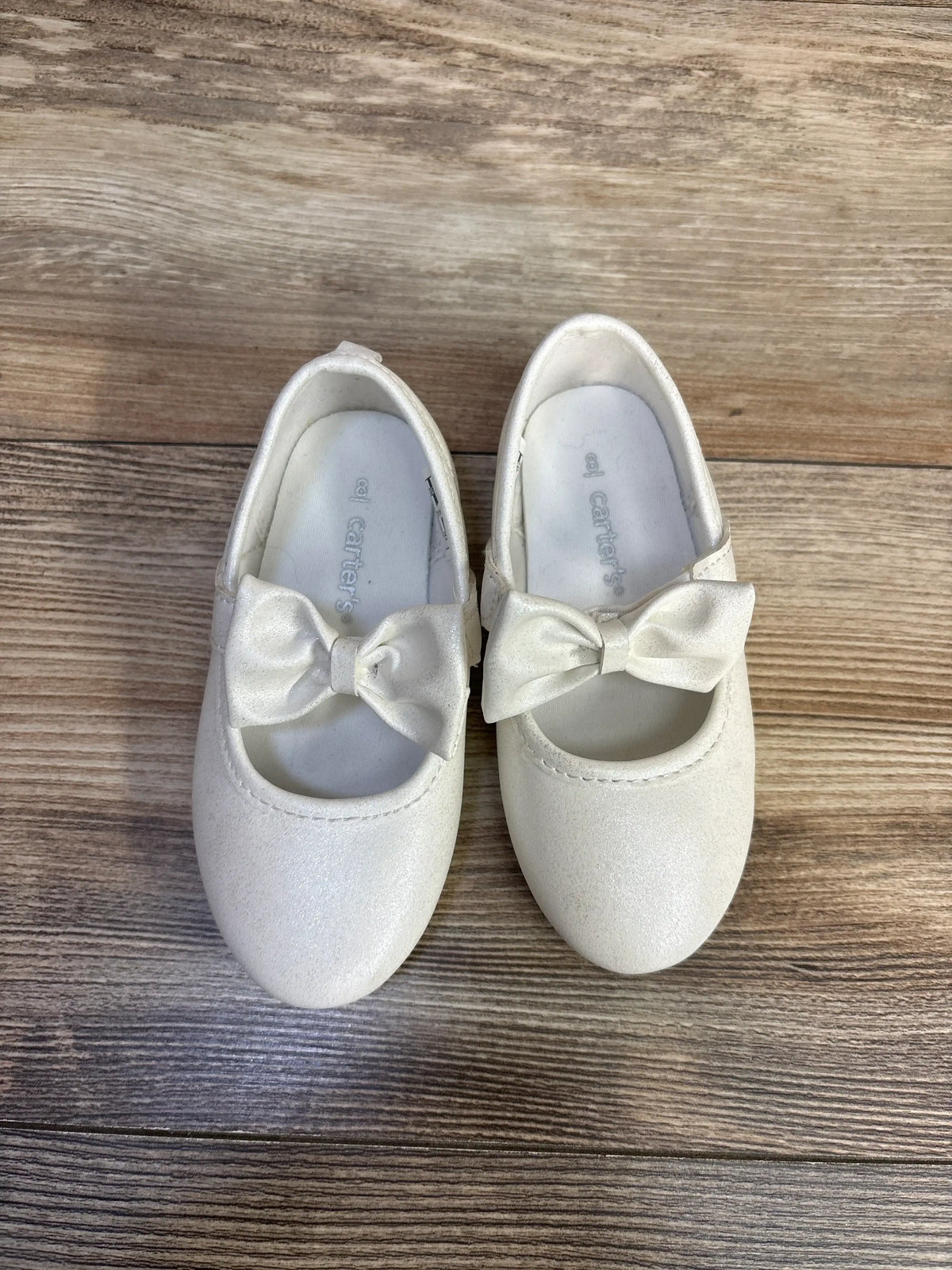 Pair of white Me n Mommy To Be classy Mary Jane flats with bows on a wooden background.