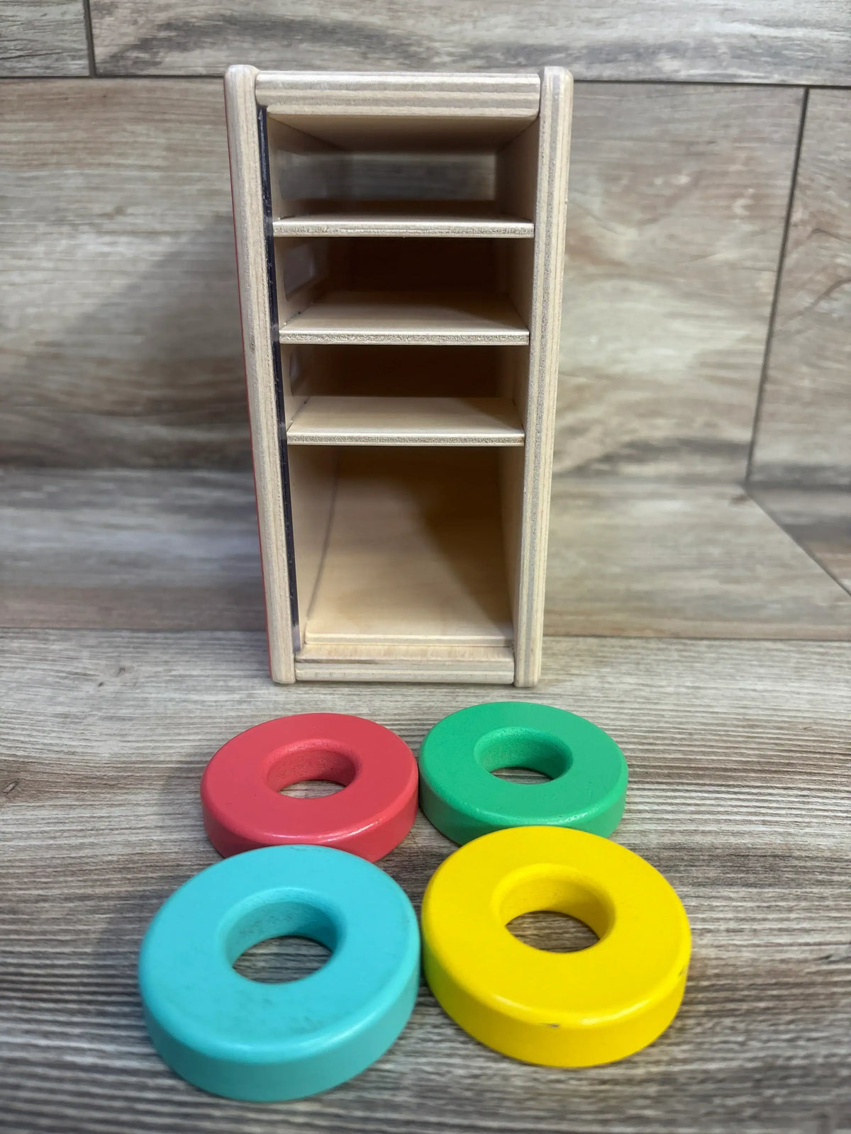 Front view of Lovevery Count & Slide Ring Chute showing four colorful wooden rings and chute shelves on a wood tabletop