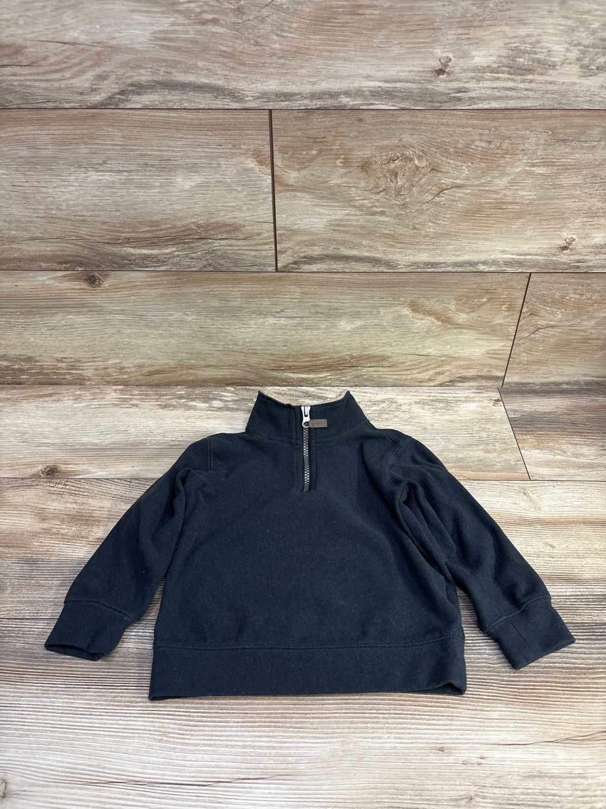 Front view of Carter’s quarter-zip sweatshirt, size 2T, showing the zipper and ribbed cuffs on a wood plank background