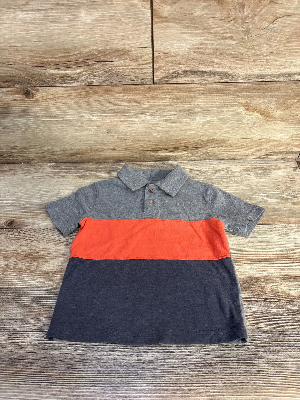 Front view of Jumping Beans polo shirt in size 12 months showcasing gray collar, red stripe, and navy lower section on wood