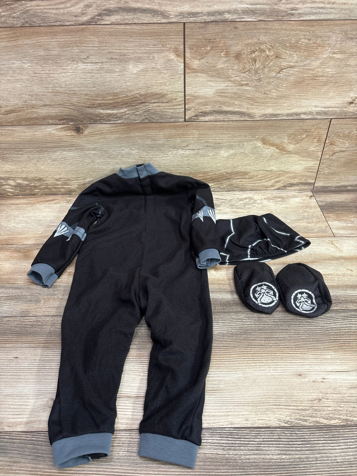 Overhead view of a black Black Panther three-piece costume showcasing gray cuffs and character graphics on a wood floor