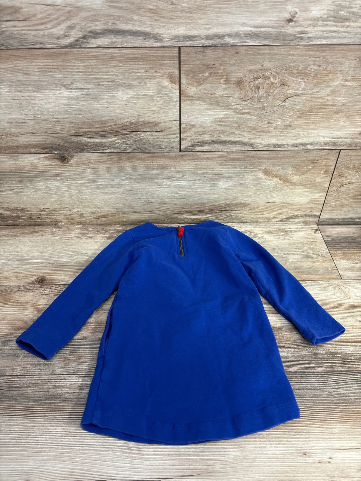 Blue long-sleeve toddler dress laid flat on wood floor background, children's clothing resale