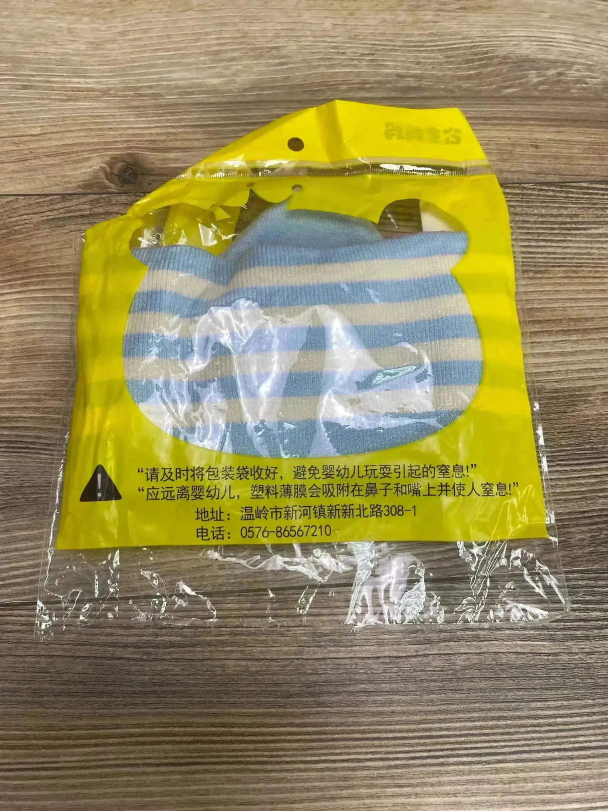 Front view of baby knit hat and matching scarf set (0-12 months) in blue and white stripes, inside yellow plastic packaging on wood surface