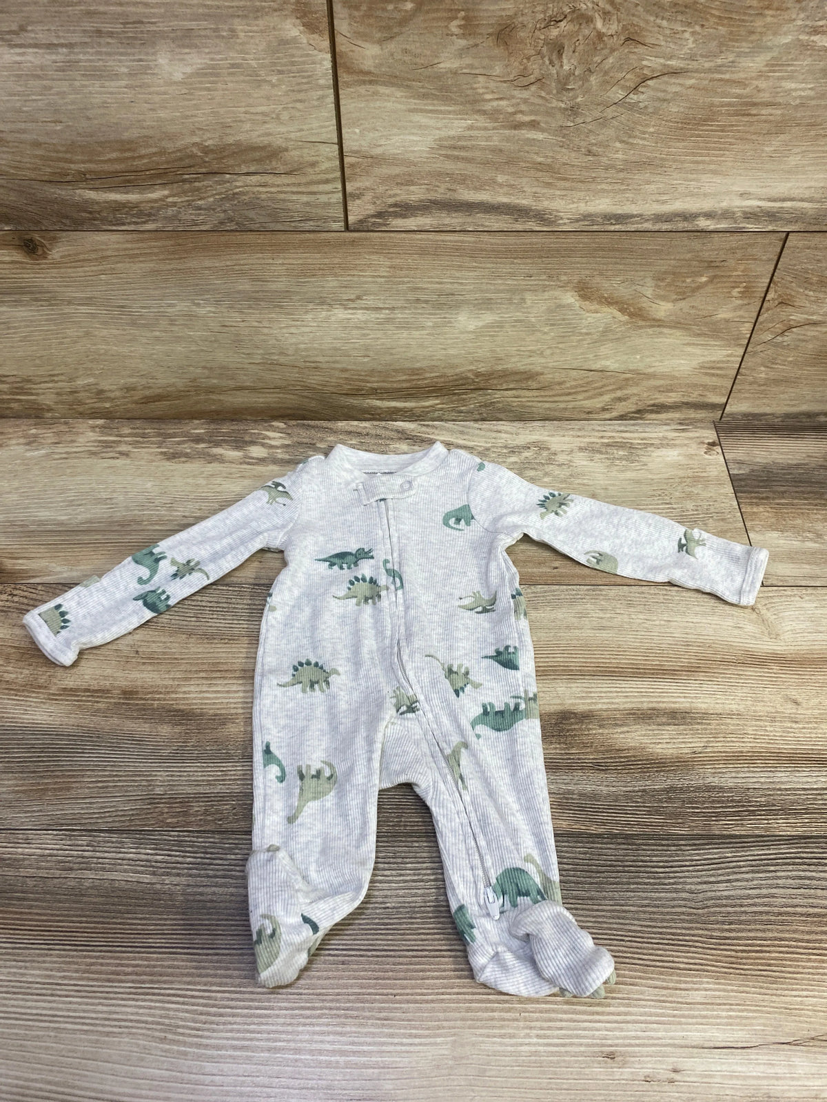 Front view of Just One You newborn sleeper showcasing gray ribbed fabric, green dinosaur print, zipper, and footed legs