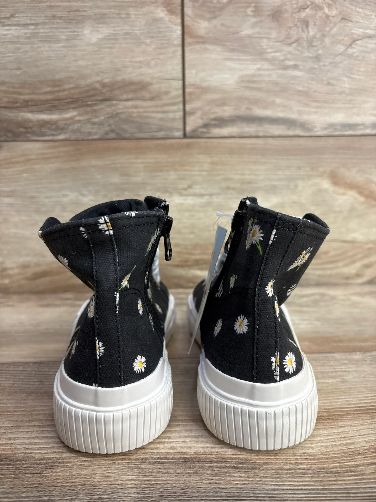 Black kids high top sneakers with white daisy print and white rubber soles on wood floor