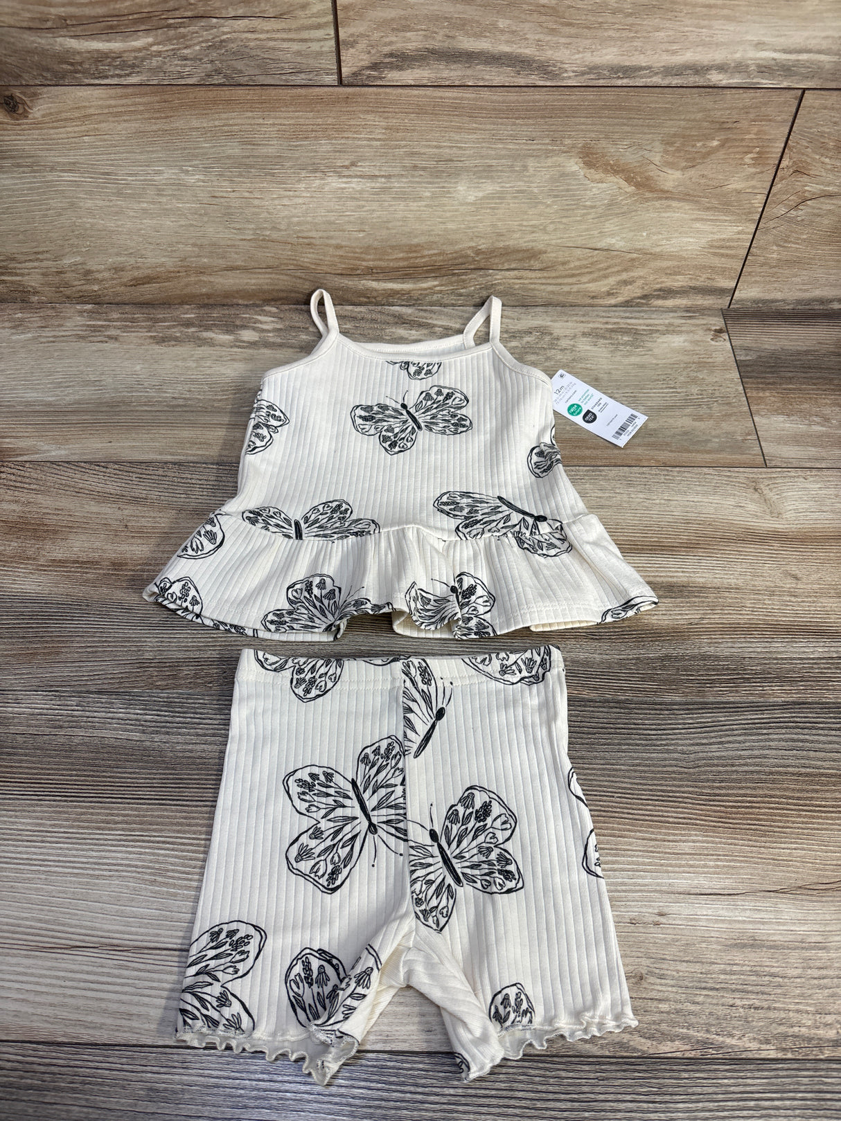 Flat lay of cream ribbed tank and shorts set, size 12m, showing black butterfly print, peplum tank and ruffled shorts on wood