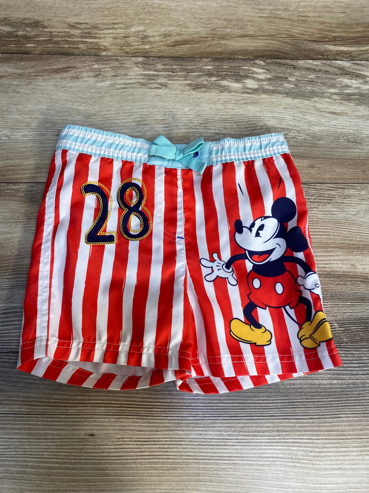 Red and white striped kids shorts with cartoon mouse graphic and number 28 on wood background