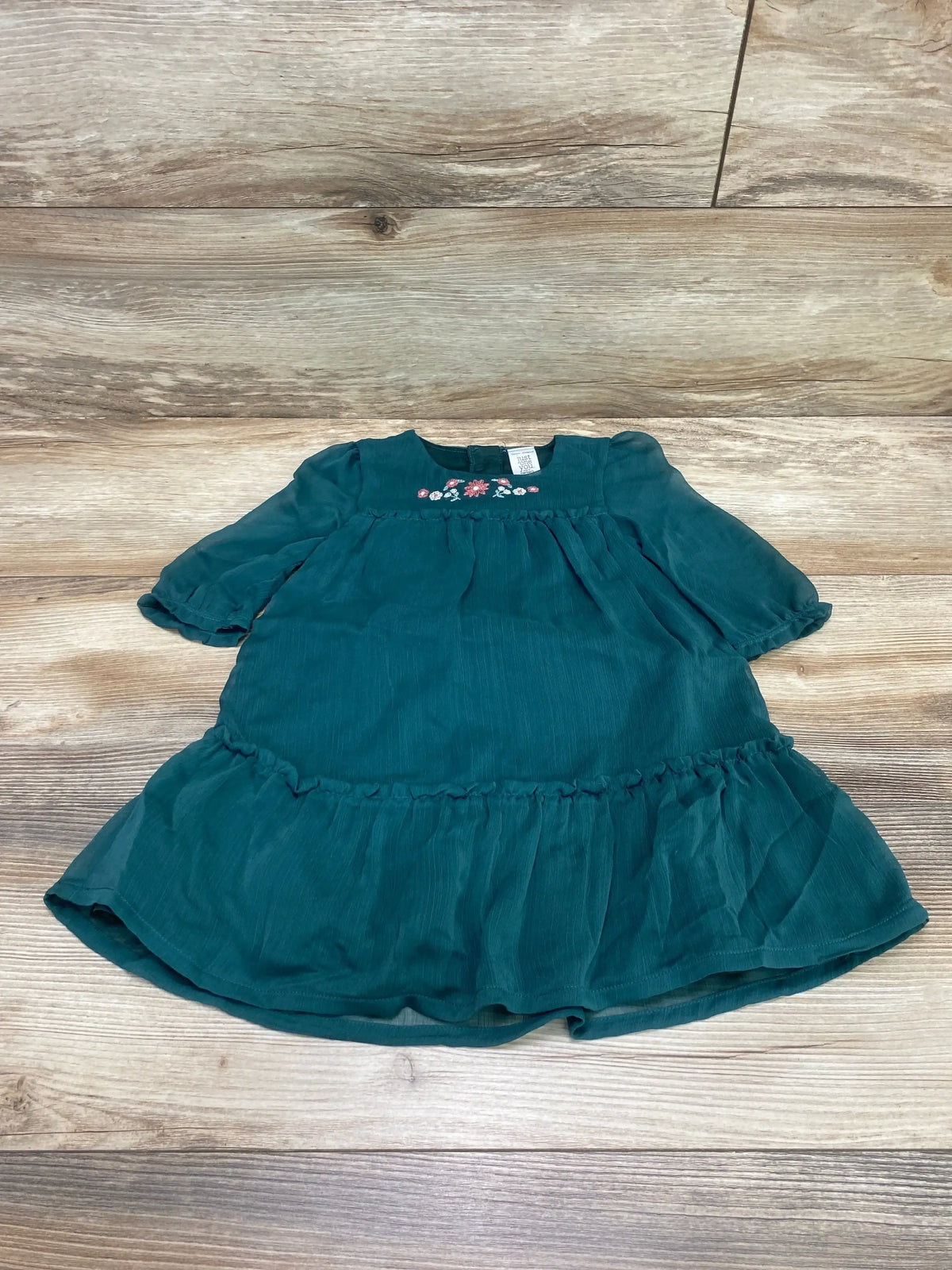 Flat lay of green toddler dress showing pink floral embroidery at chest, puff sleeves and ruffled hem on wood background