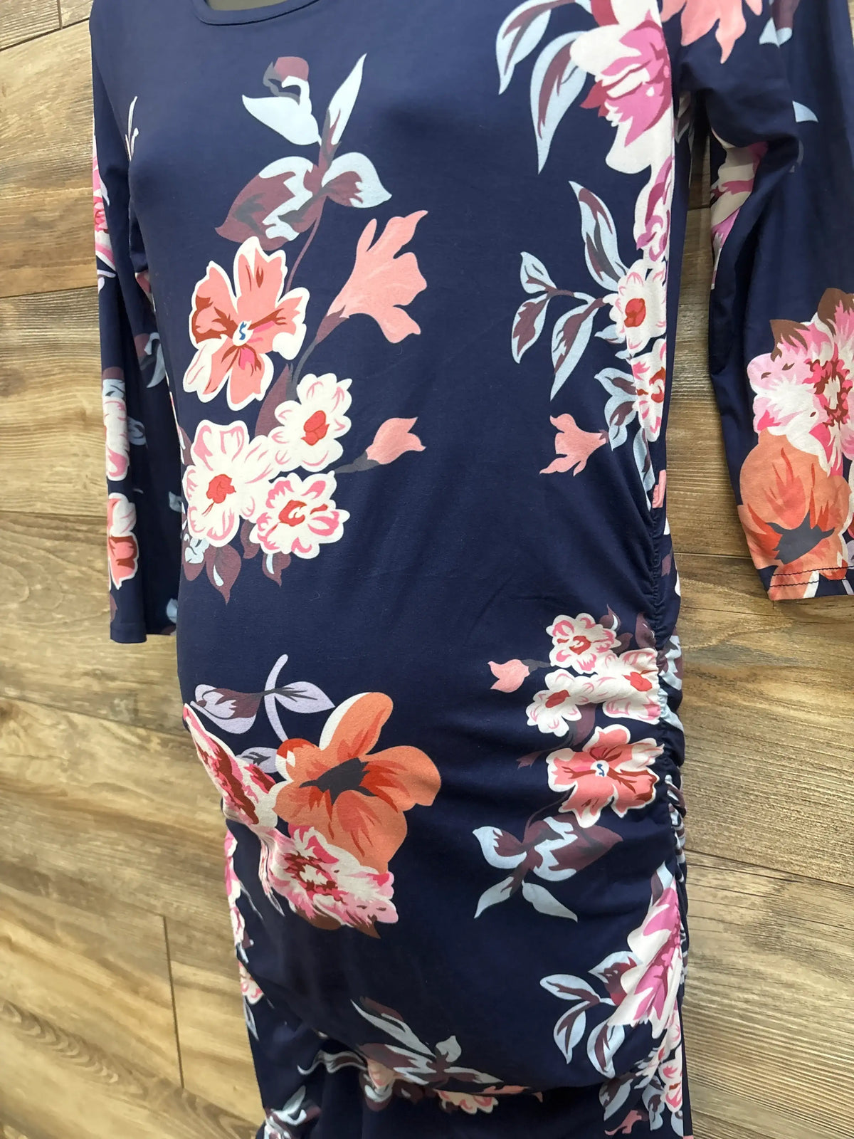 Front view of Miss Qee maternity floral bodycon dress showcasing navy floral print and ruched sides on a wood floor