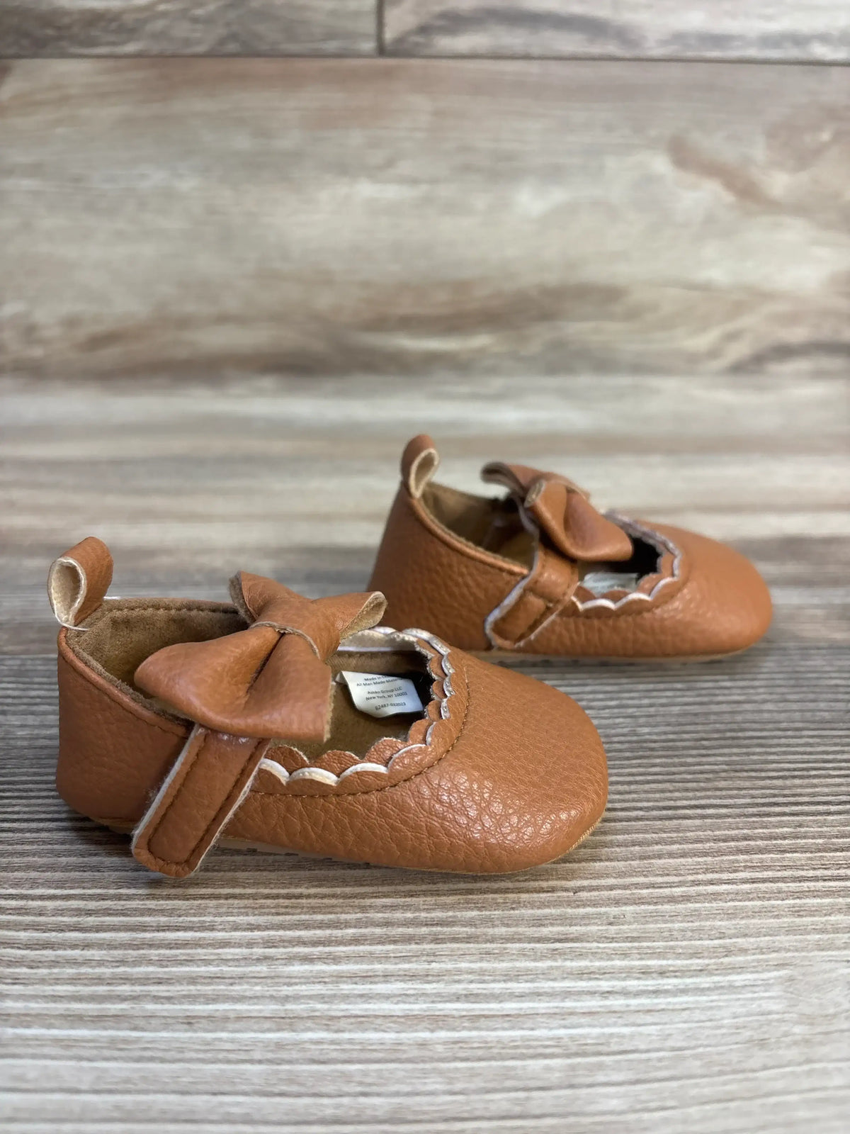 Brown leather baby shoes with bow detail on wood background, gently used kids footwear