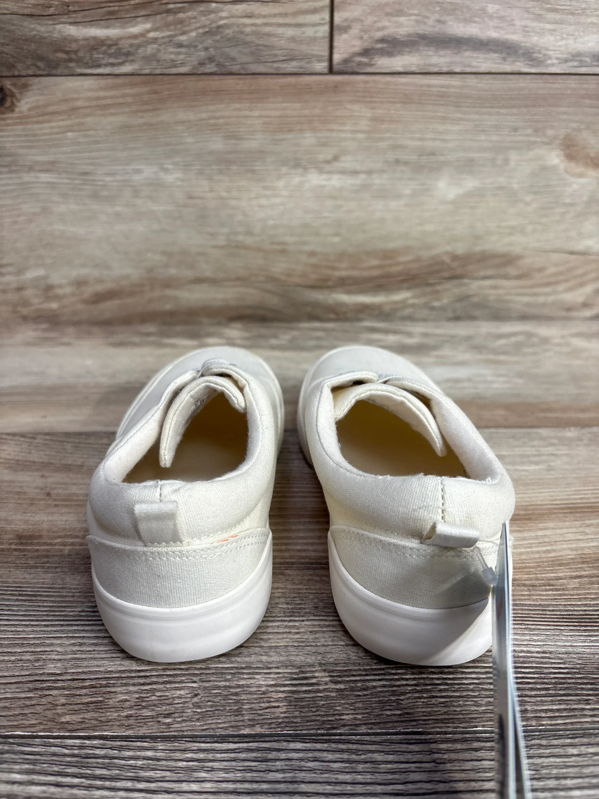 Back view of white toddler canvas shoes with rubber soles on wood floor