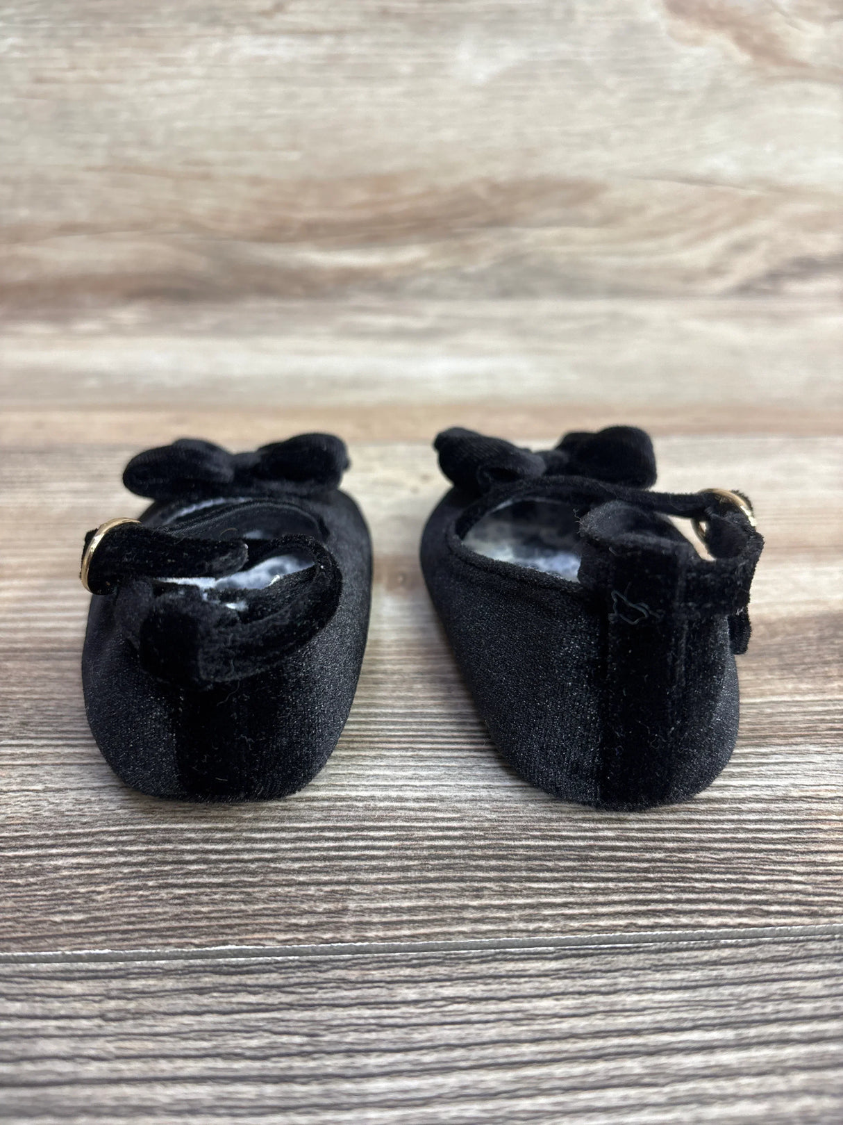 Black velvet baby Mary Jane shoes with bows on wooden surface