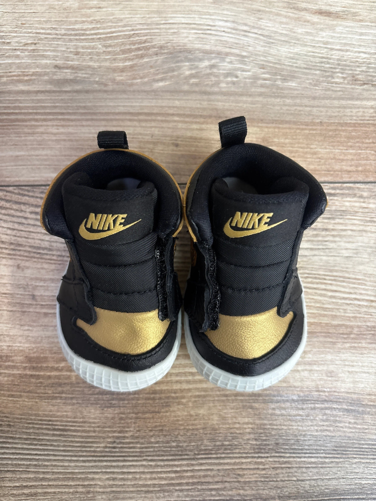 Pair of black and gold Nike baby shoes on wooden floor for kids resale