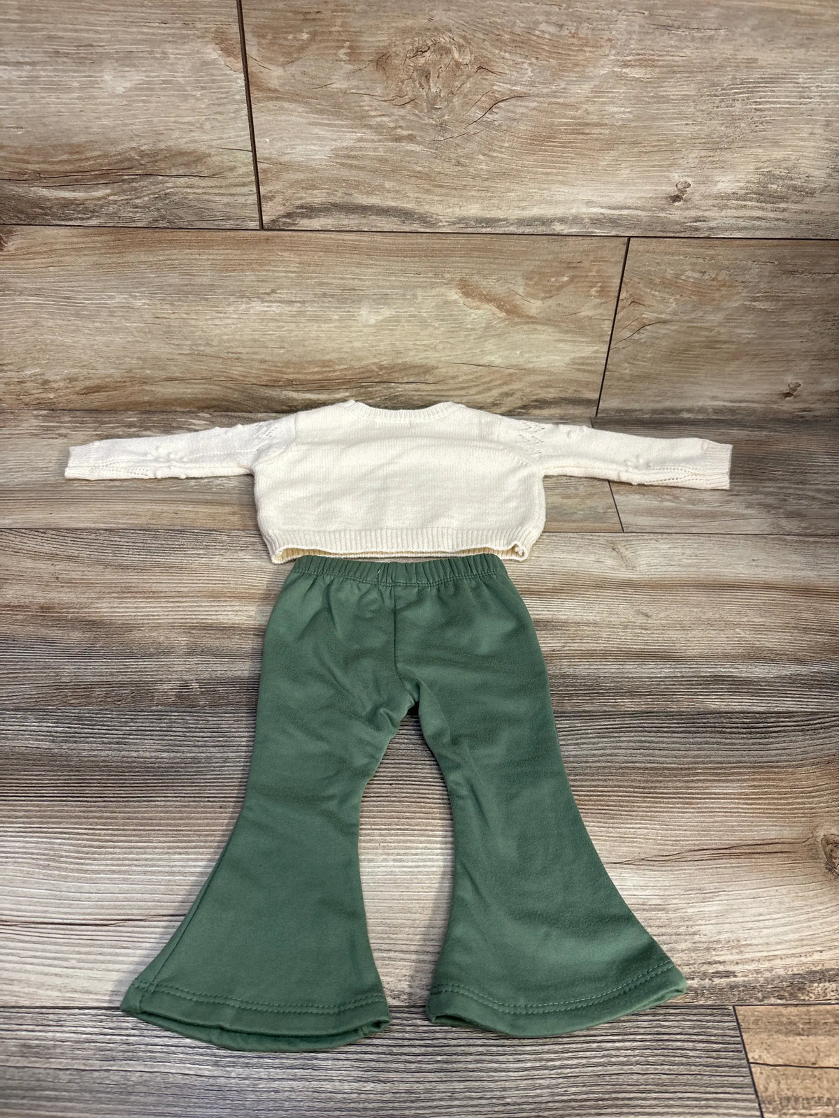 Top-down view of cream Btween baby knit sweater and flare leggings set showcasing flared legs on a wood floor