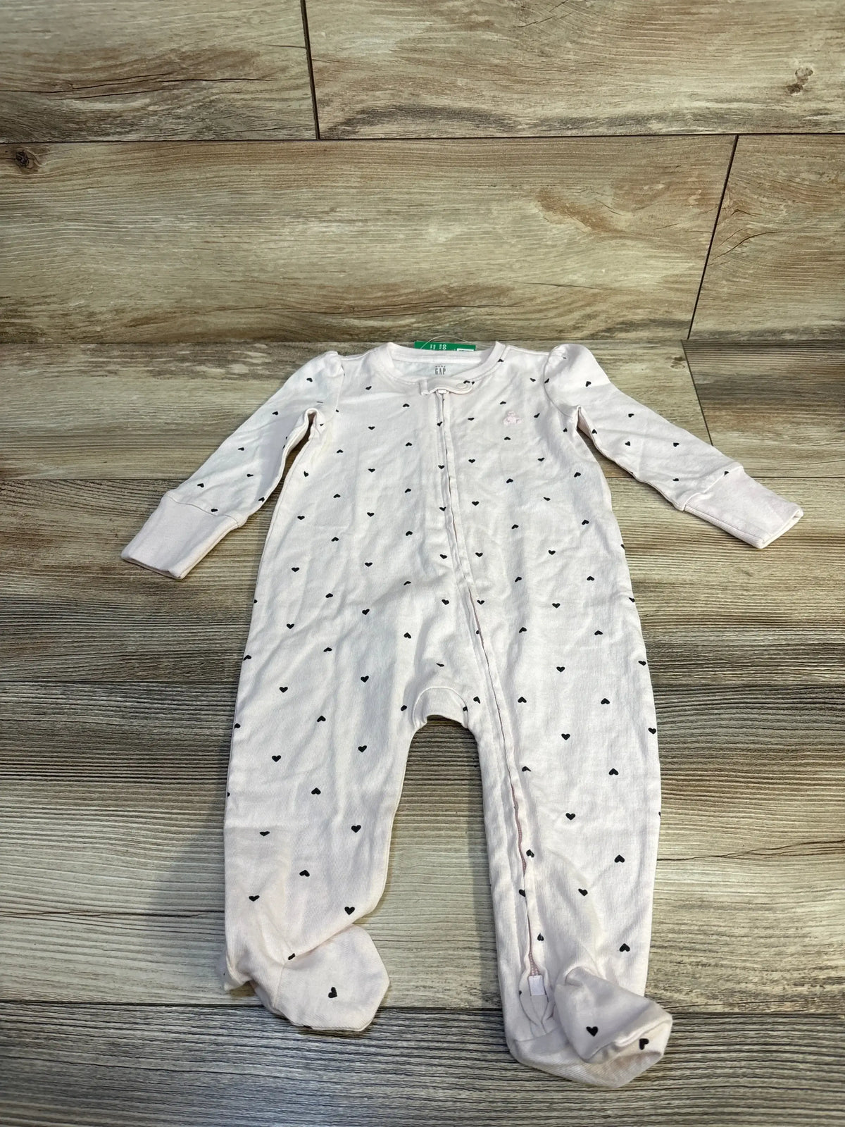 Light pink baby sleeper with black heart print, long sleeves, and zip closure on wood background