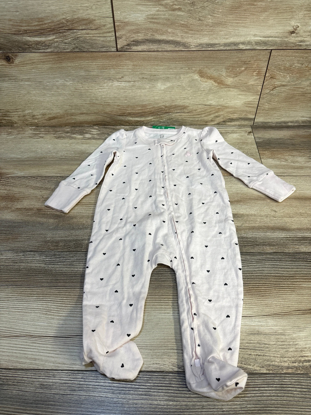 Light pink baby sleeper with black heart print, long sleeves, and zip closure on wood background