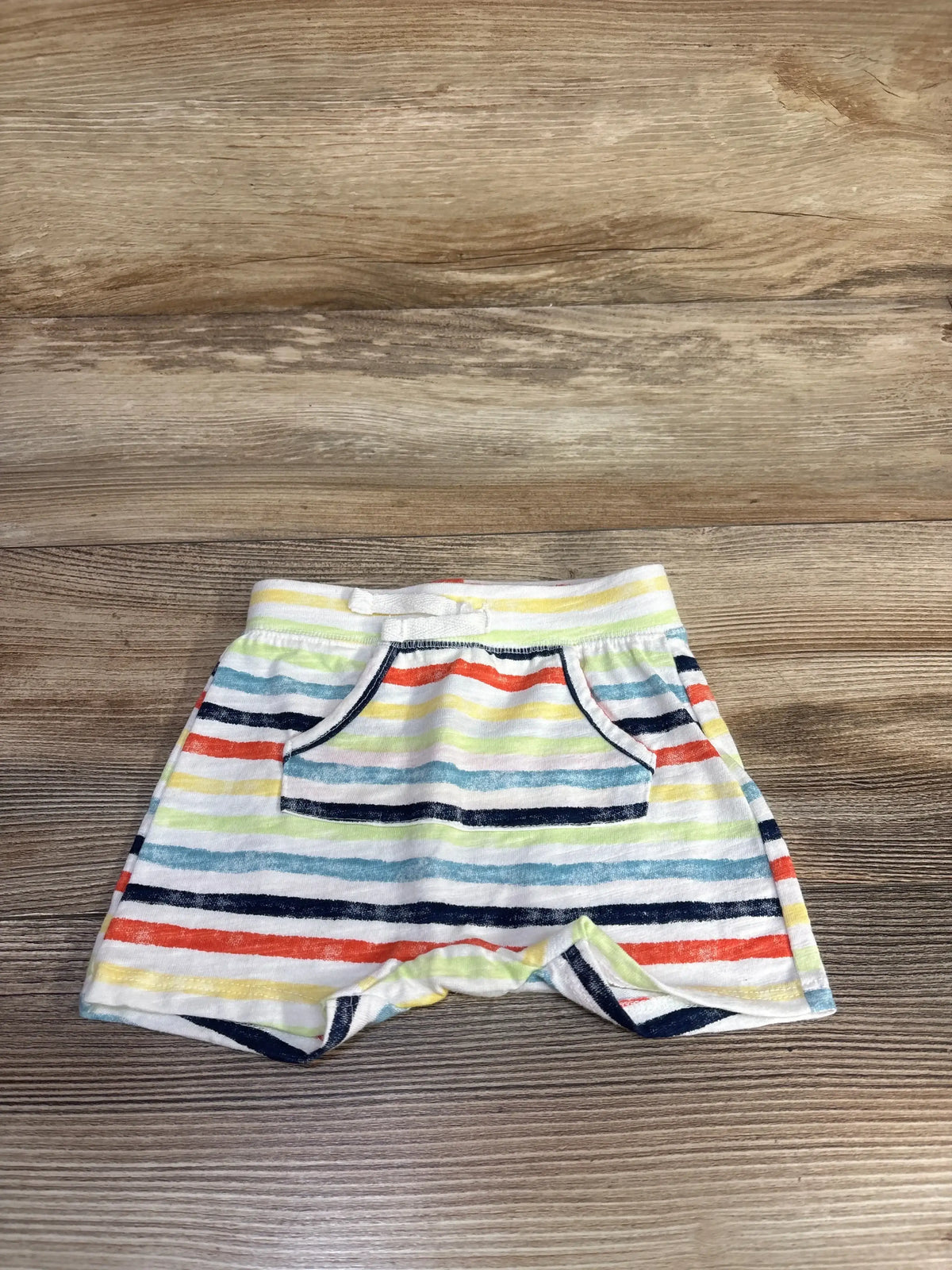 Flat lay of Jumping Beans baby striped shorts (white) showing front kangaroo pocket and elastic waistband with drawstring on wood background