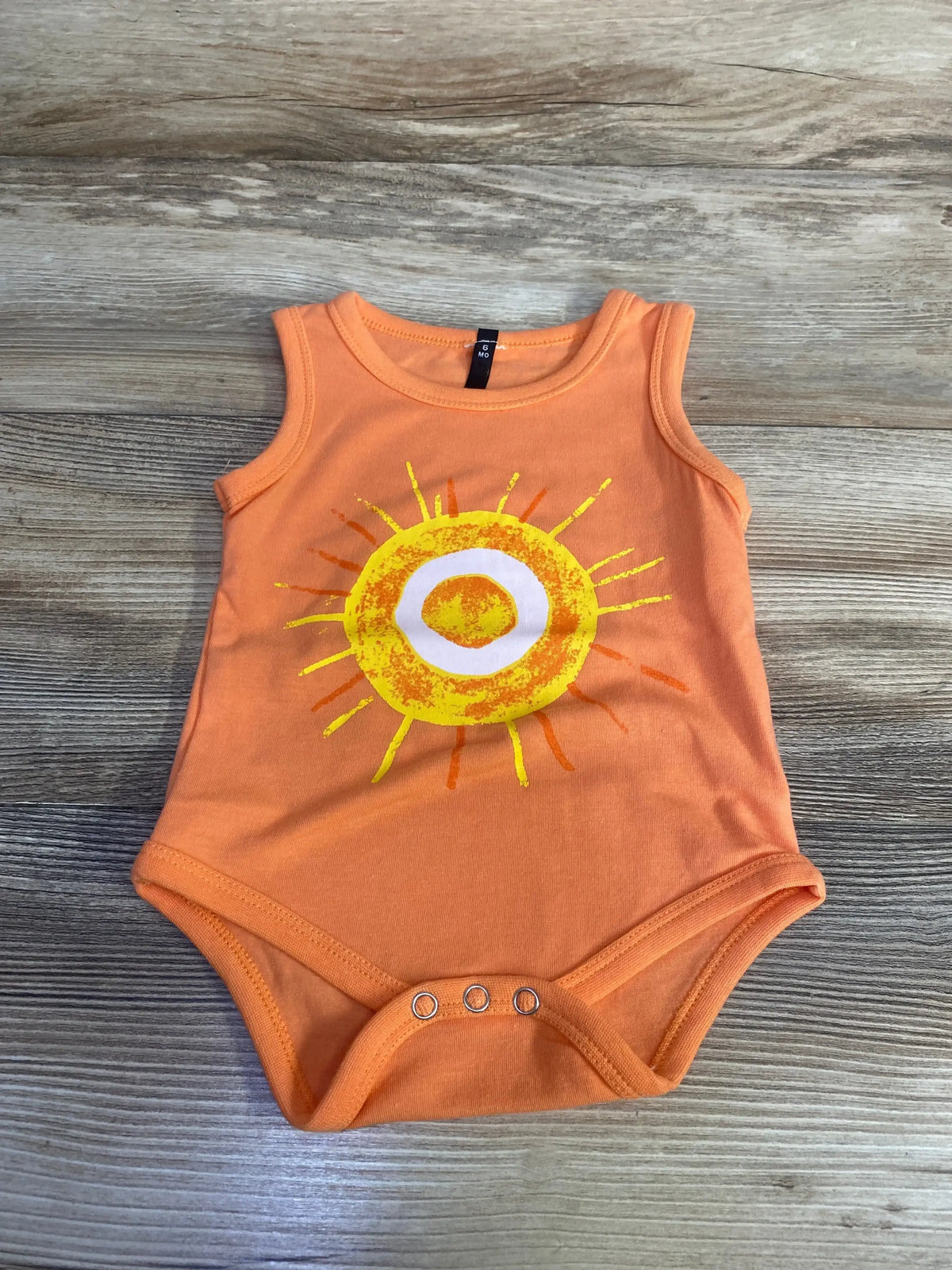 Front flat lay of orange baby tank bodysuit, size 6 months, showing yellow sun print and three crotch snaps on light wood background