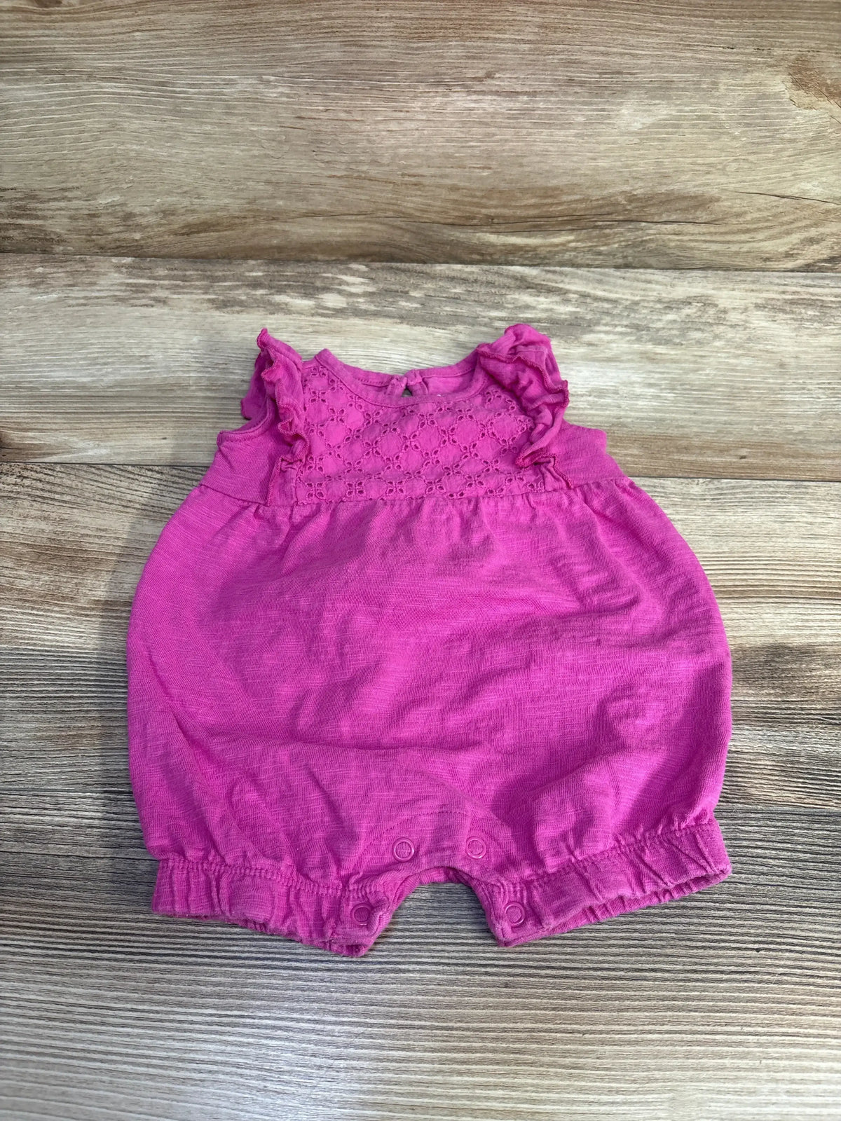 Top down view of Just One You romper in pink with eyelet lace yoke, ruffle sleeves and snap leg closures on wood background