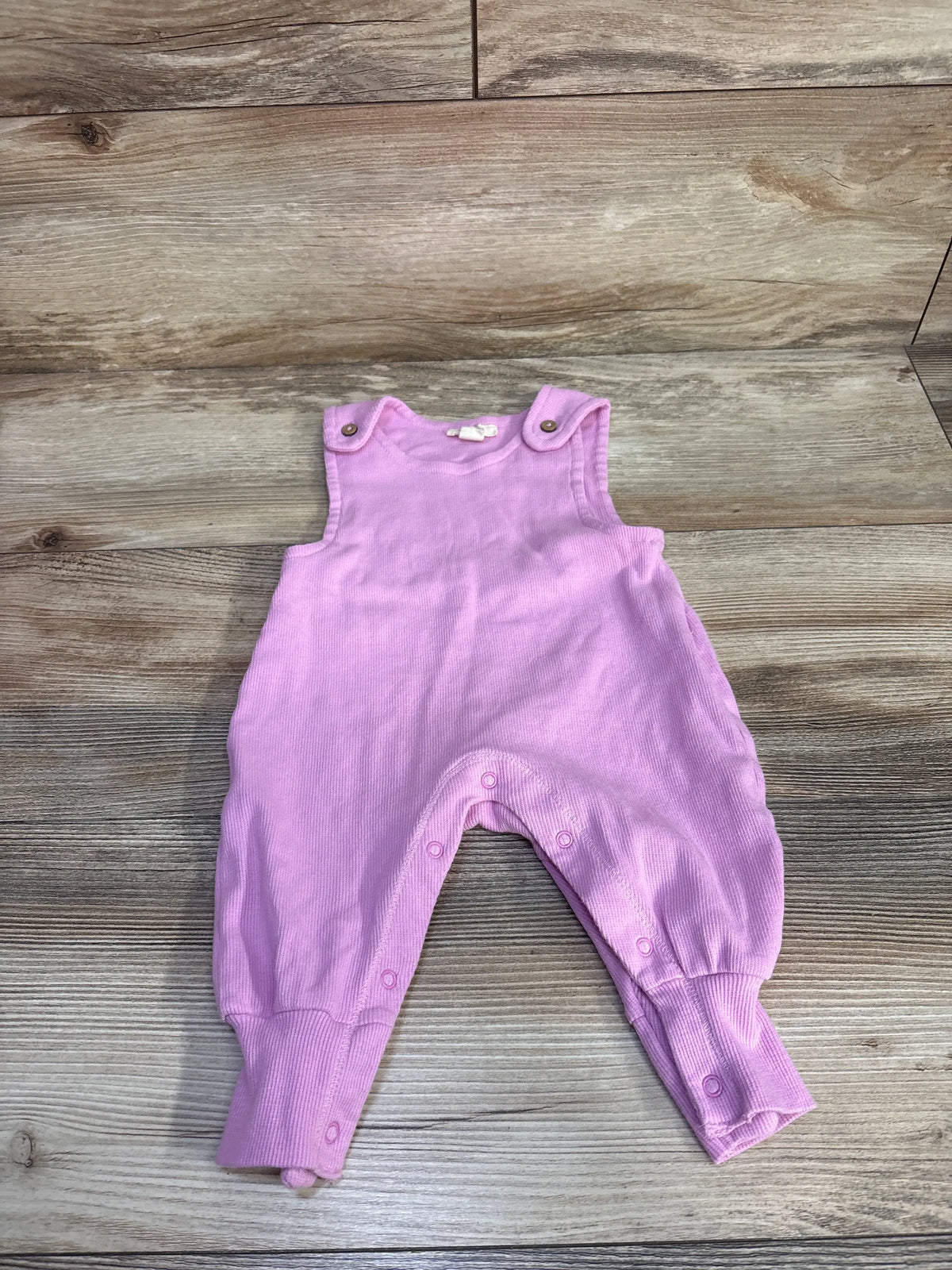 Front view of Burt’s Bees Baby pink sleeveless ribbed jumpsuit showcasing shoulder and leg snaps on a wood-look background