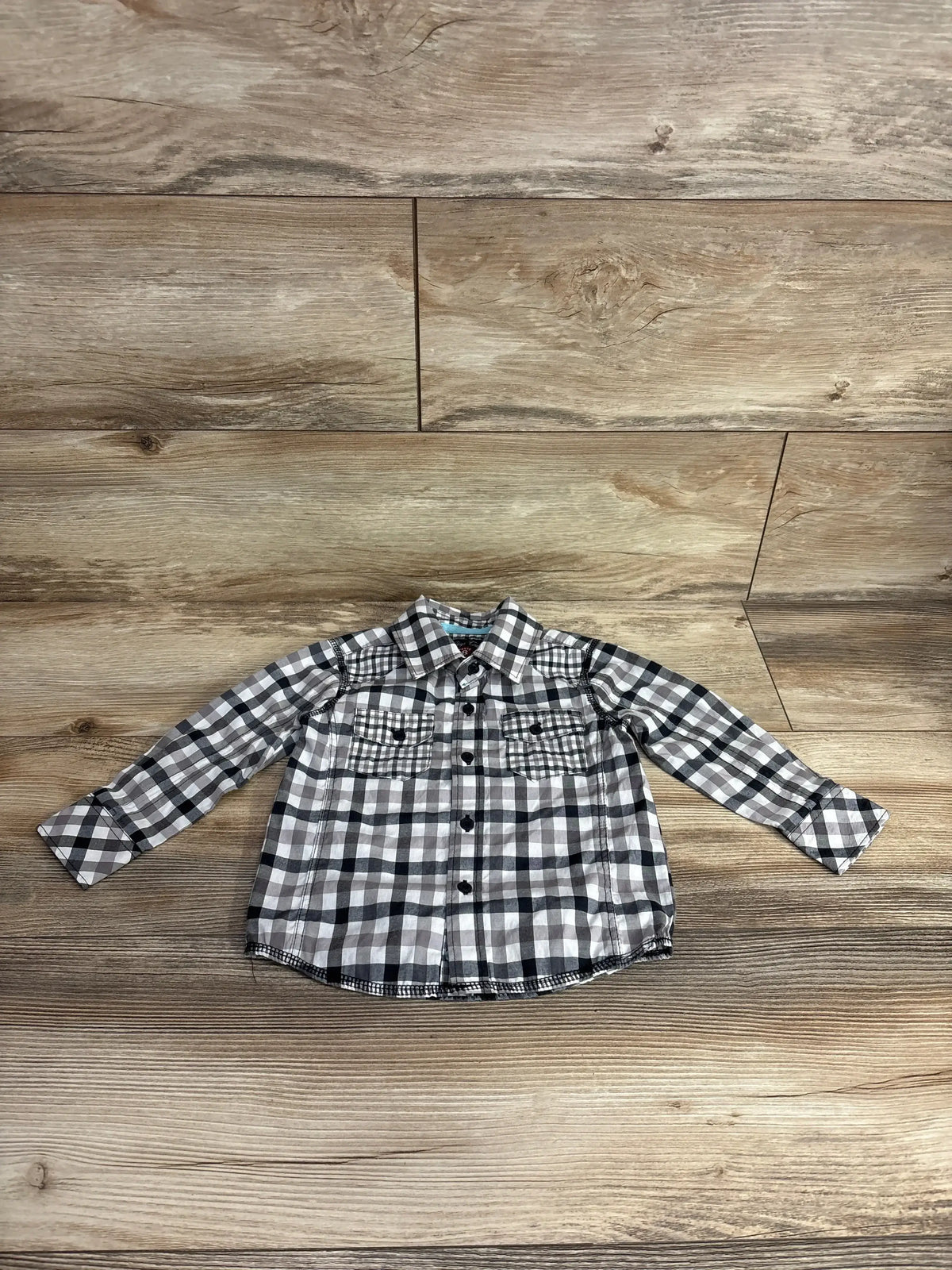 Children's long-sleeve black and white plaid button-up shirt on wooden floor