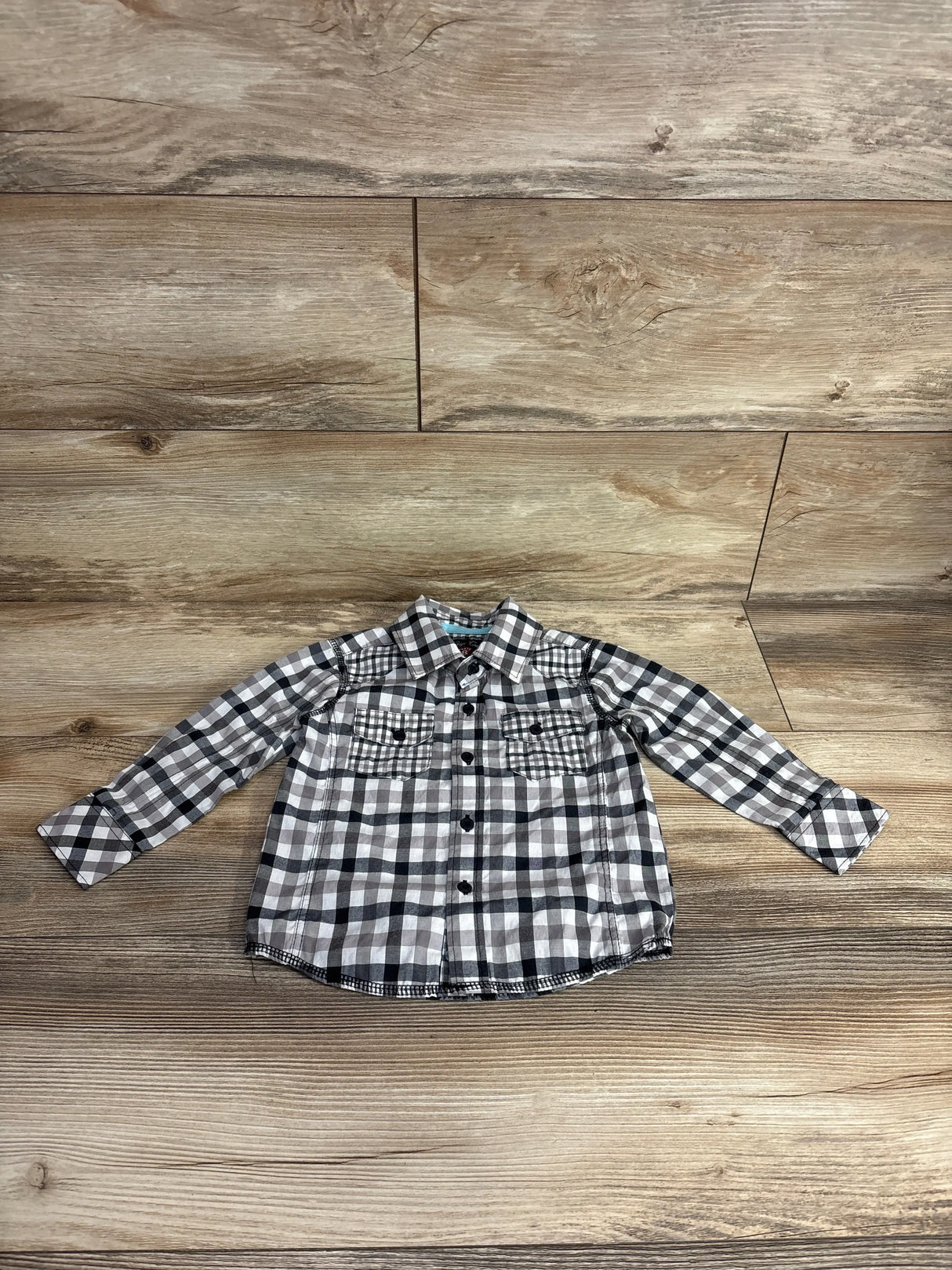 Children's long-sleeve black and white plaid button-up shirt on wooden floor