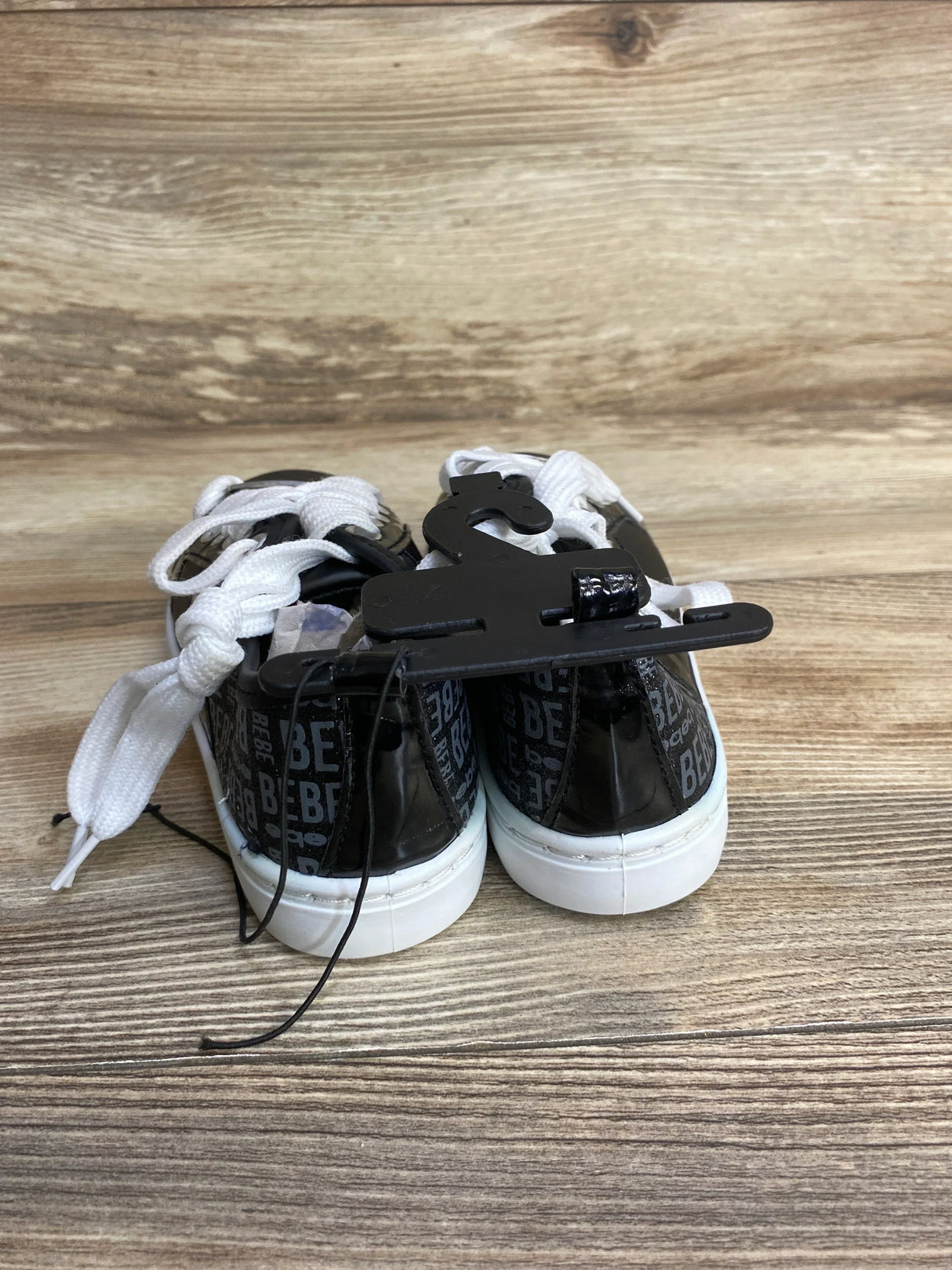 Back view of black Bebe sneakers with white laces on wood surface