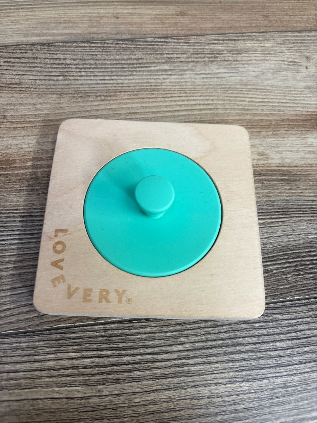 Top down view of Lovevery wooden Montessori baby puzzle showing single green knobbed circle in light wood frame on wood floor