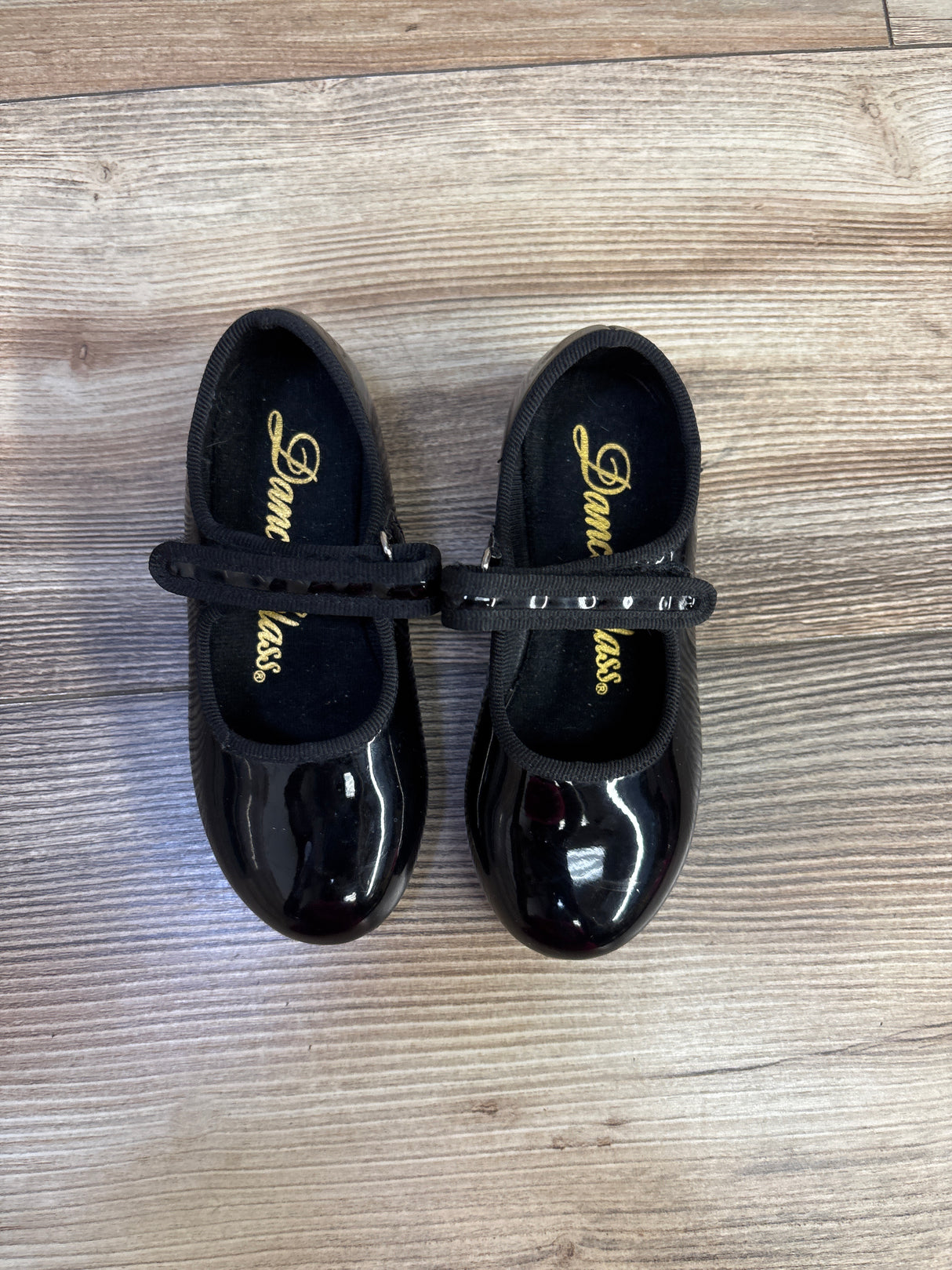 Top view of black Dance Class tap shoes size 7.5c showcasing glossy toes and secure straps on a wood look floor