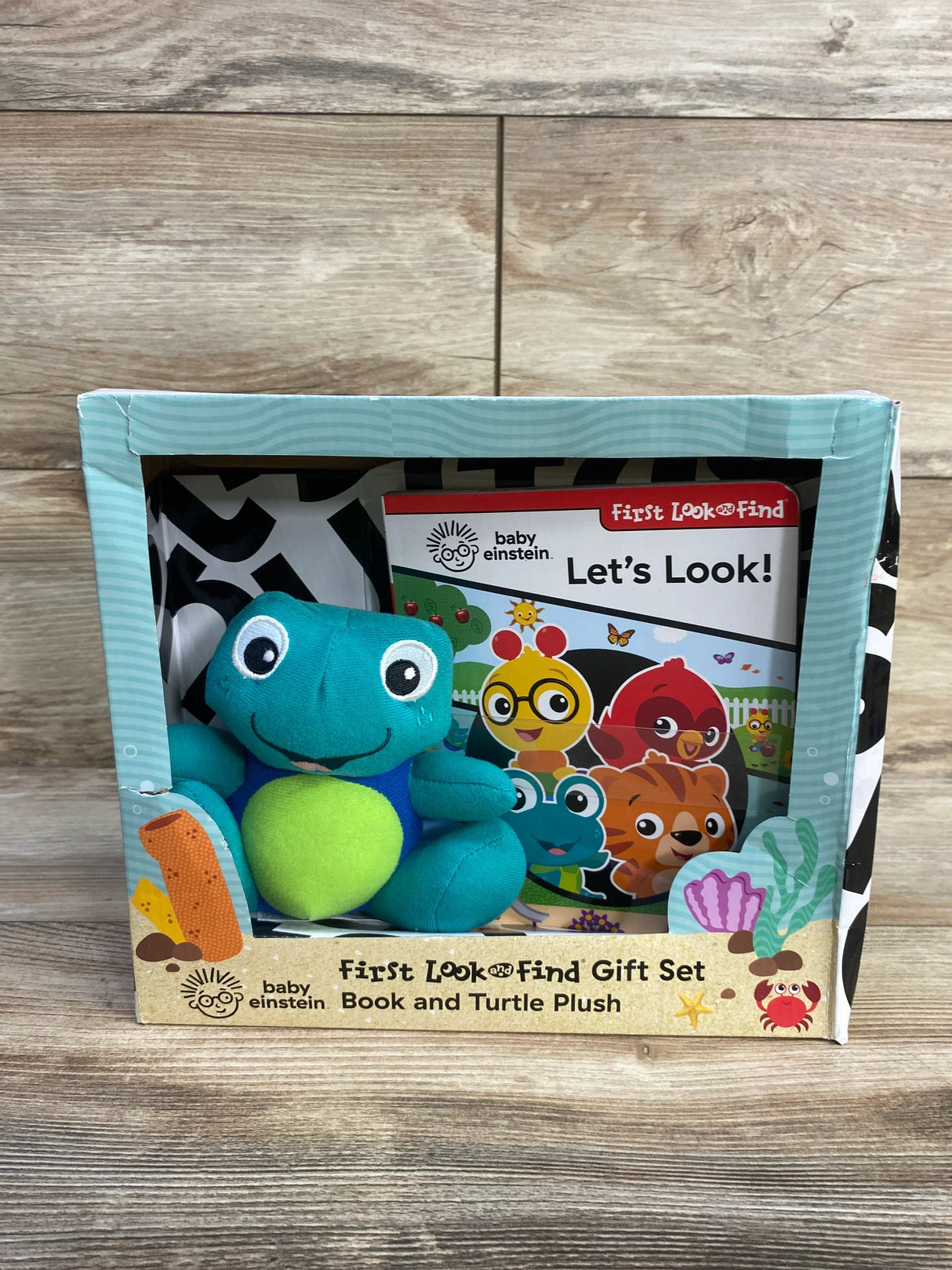 Front view of Baby Einstein First Look and Find set showing teal turtle plush and the Let's Look board book on a wood tabletop