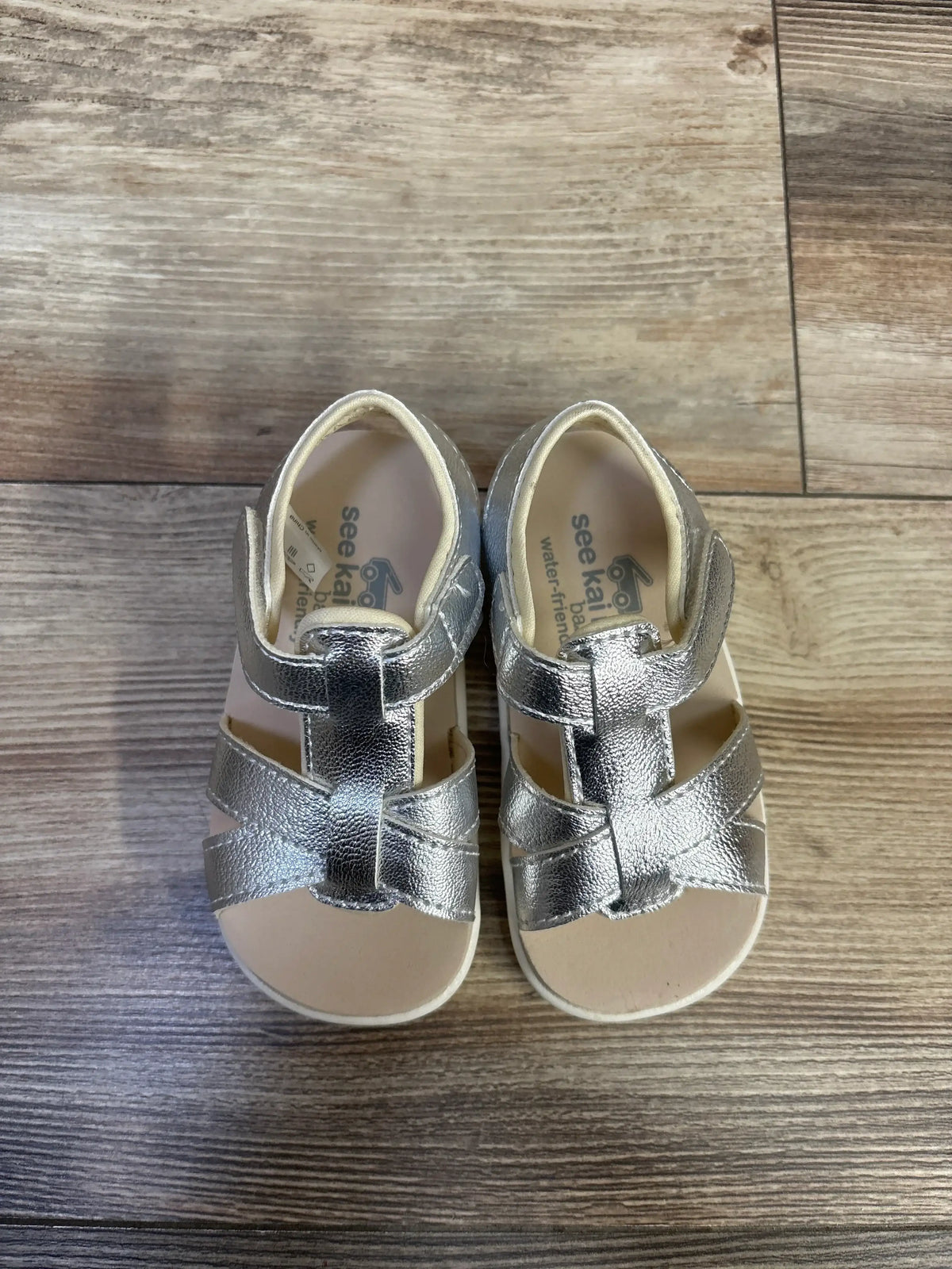 Top view of See Kai Run Shayna sandals in silver metallic, size 6C, showcasing strappy adjustable uppers on wood background