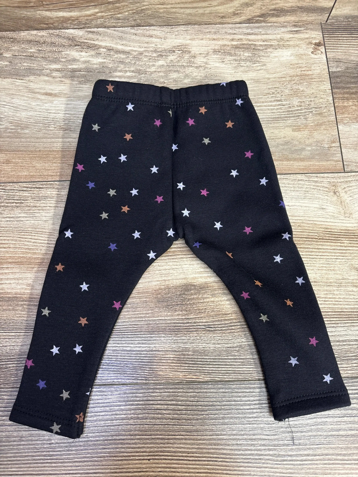 Black toddler leggings with multicolor star print on wooden floor background