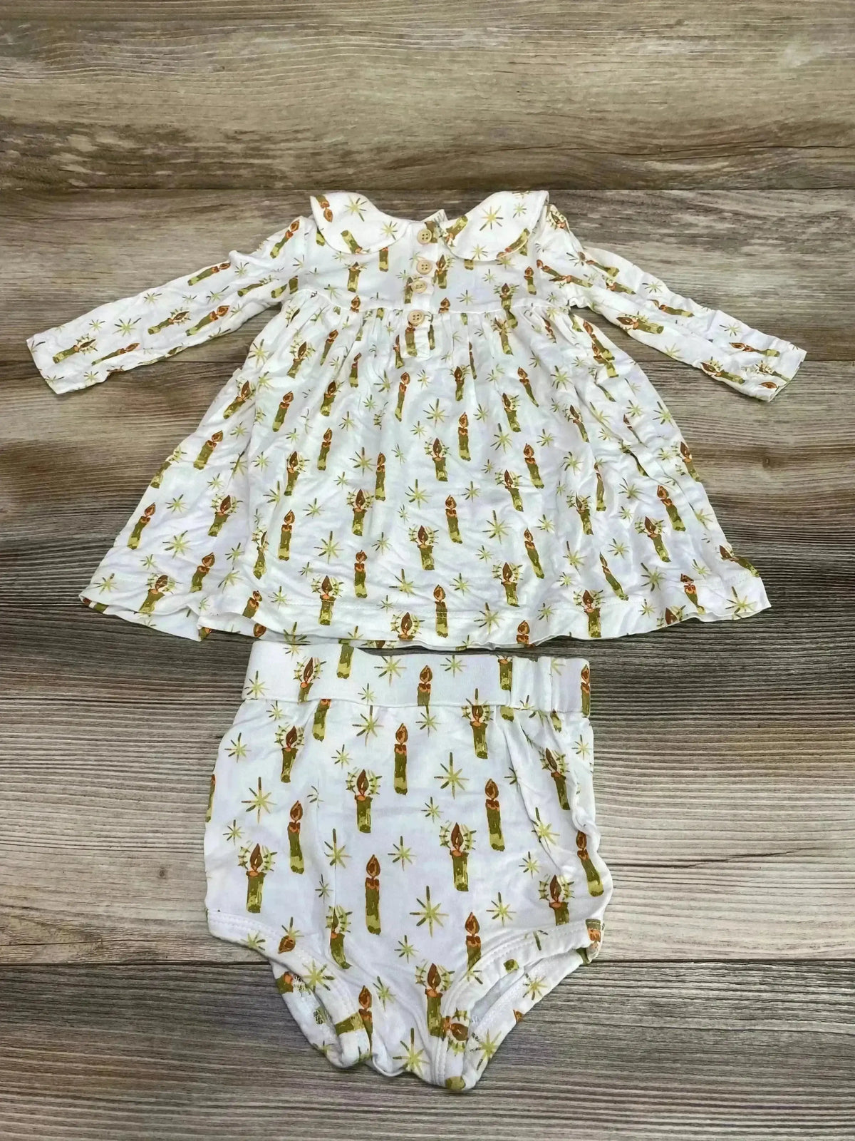 Flat lay of baby long-sleeve Peter Pan dress with matching bloomer showcasing green candle print on white fabric with wood background