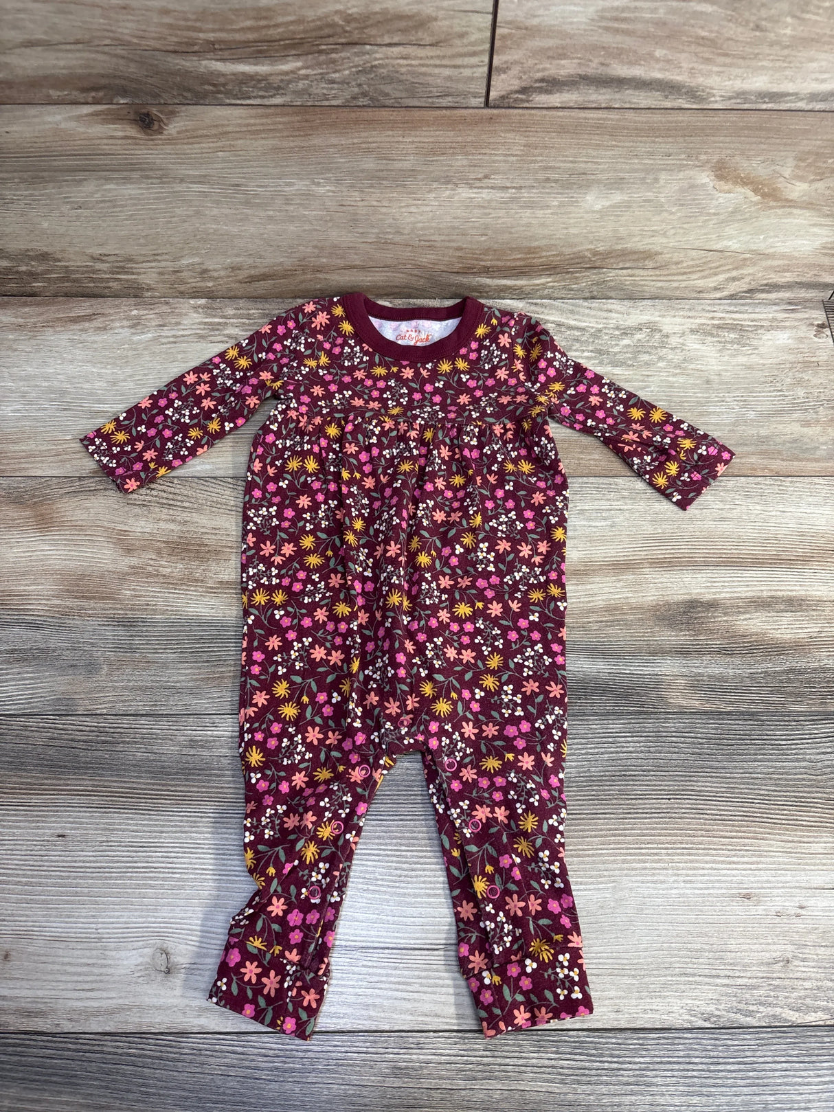 Baby romper with long sleeves, floral print in pink, yellow, white on wood floor