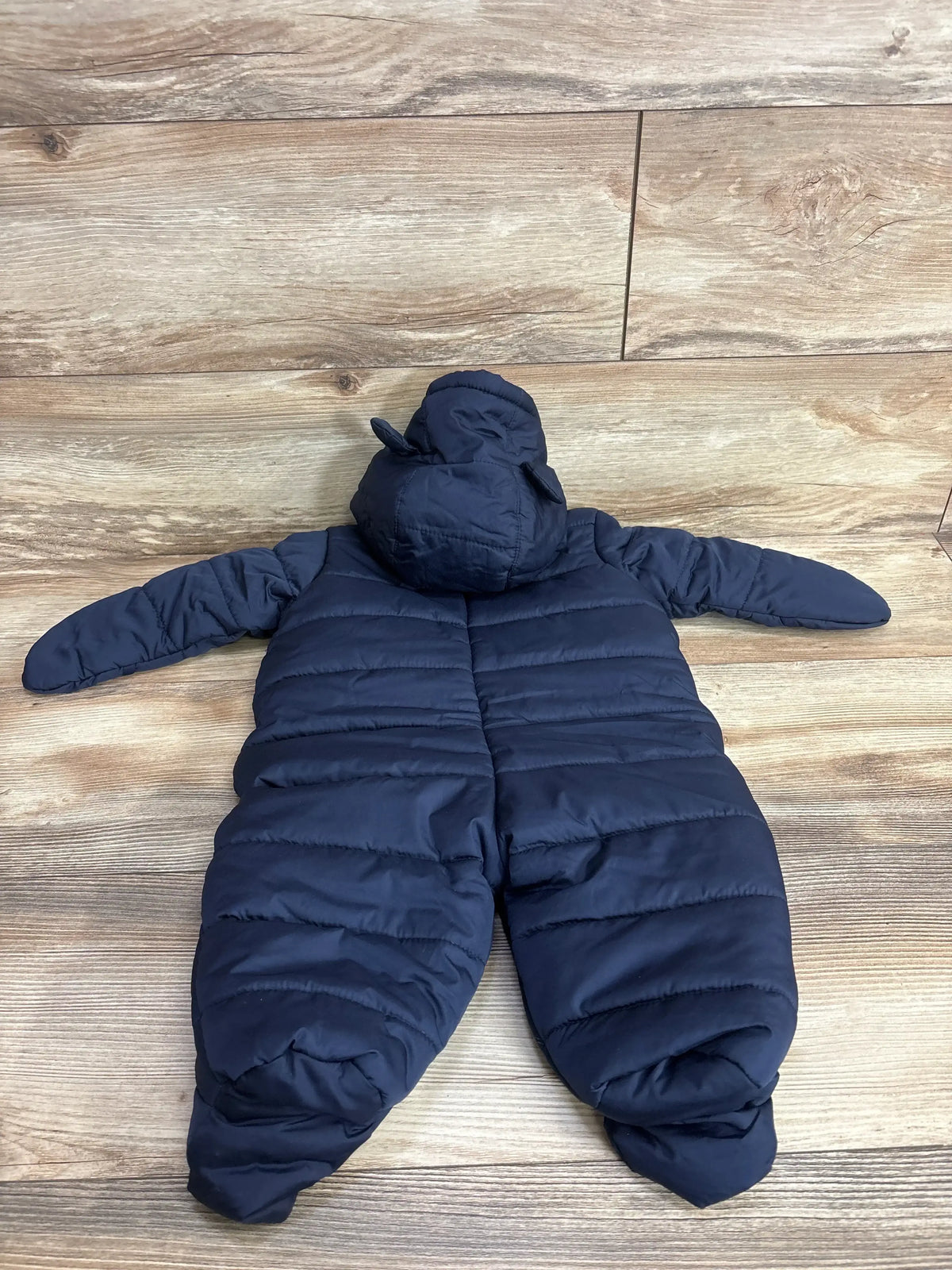 Navy blue puffer snowsuit for baby or toddler, hooded with ear details, laid flat on wood floor