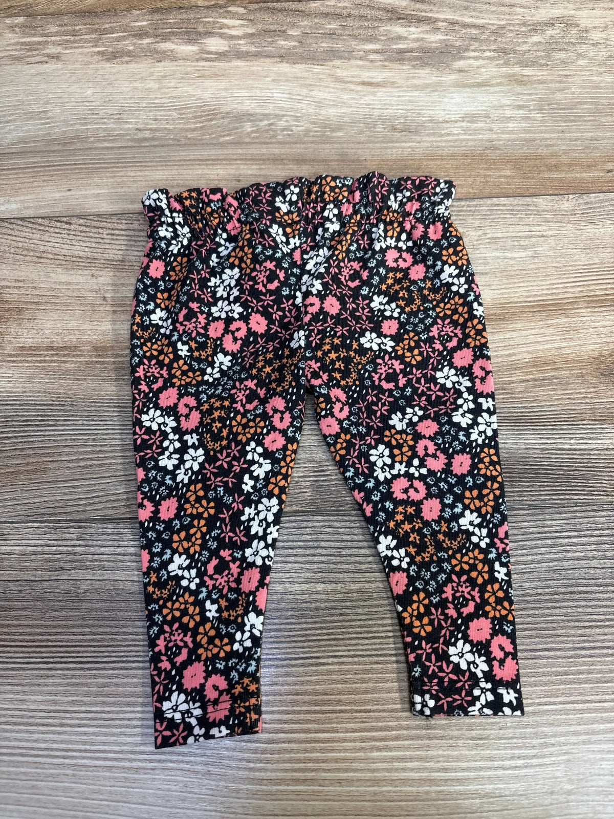Black baby leggings with pink, orange, and white floral pattern on wooden floor background